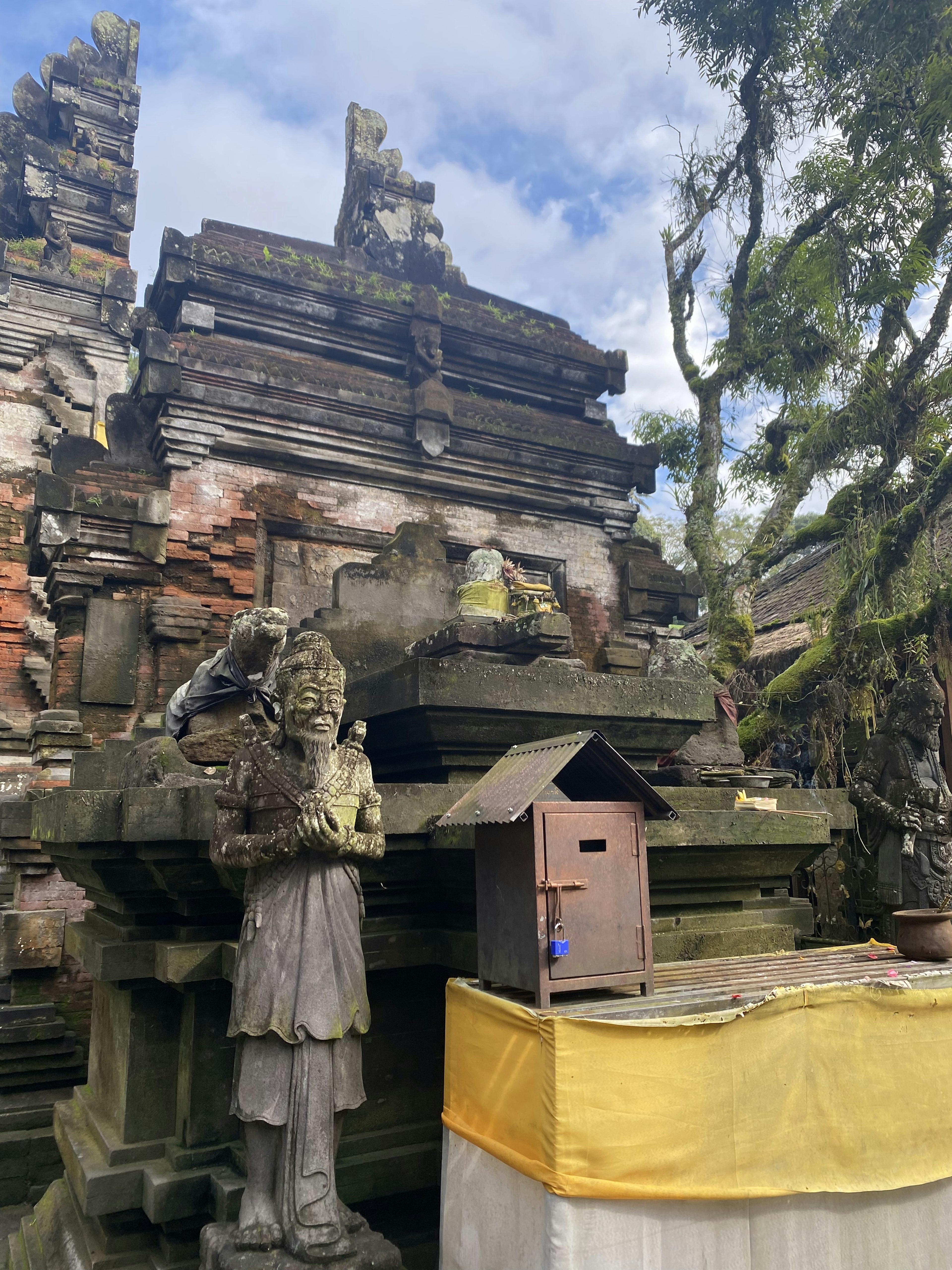 A Balinese temple scene featuring intricate stone carvings and an altar with yellow draping