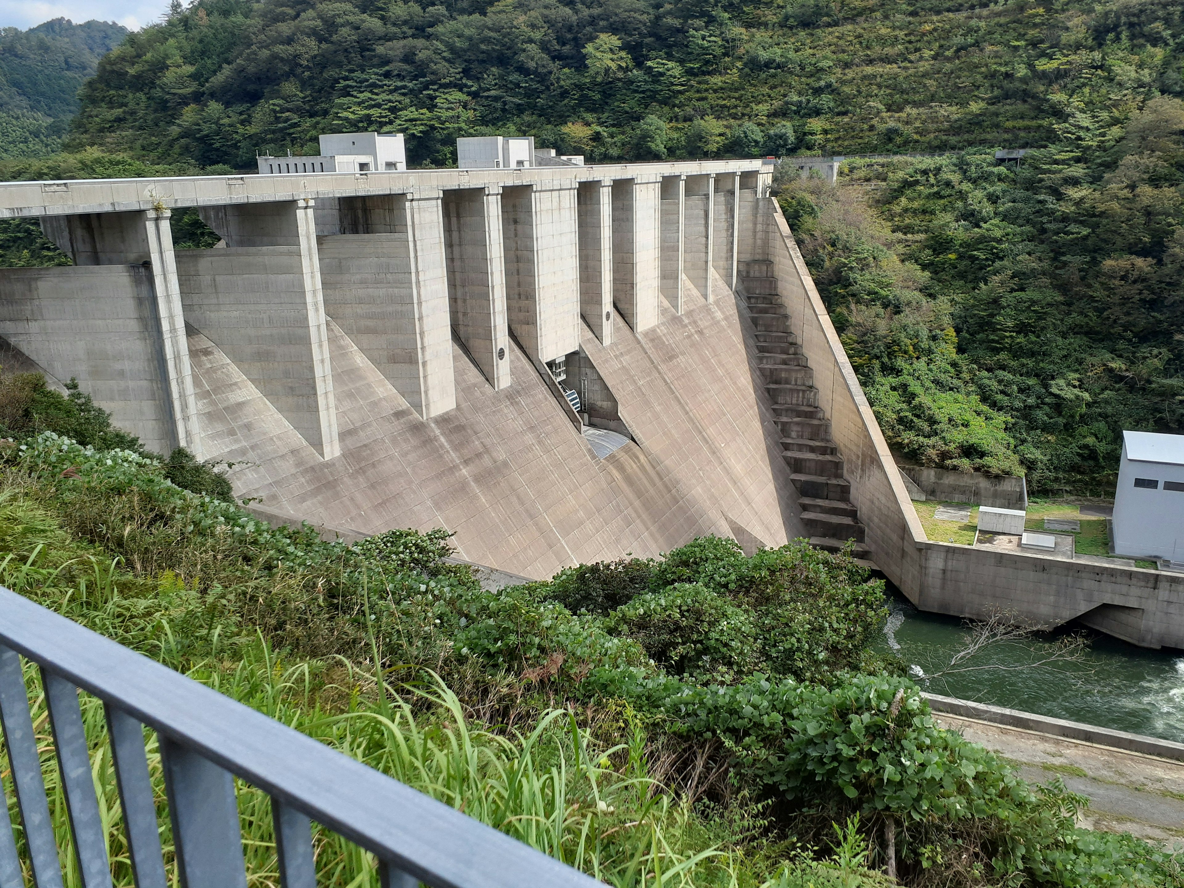 Represa de concreto con montañas verdes de fondo