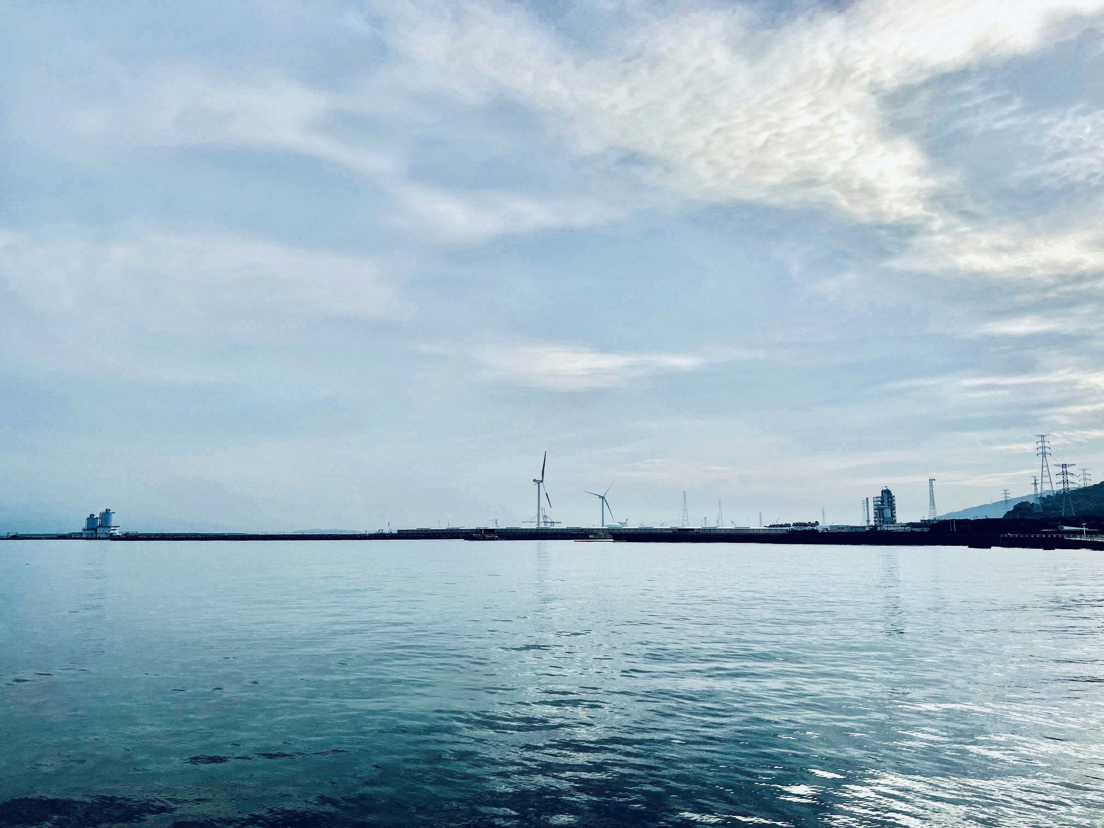 平靜的海面和多雲的天空，能看到風力渦輪機