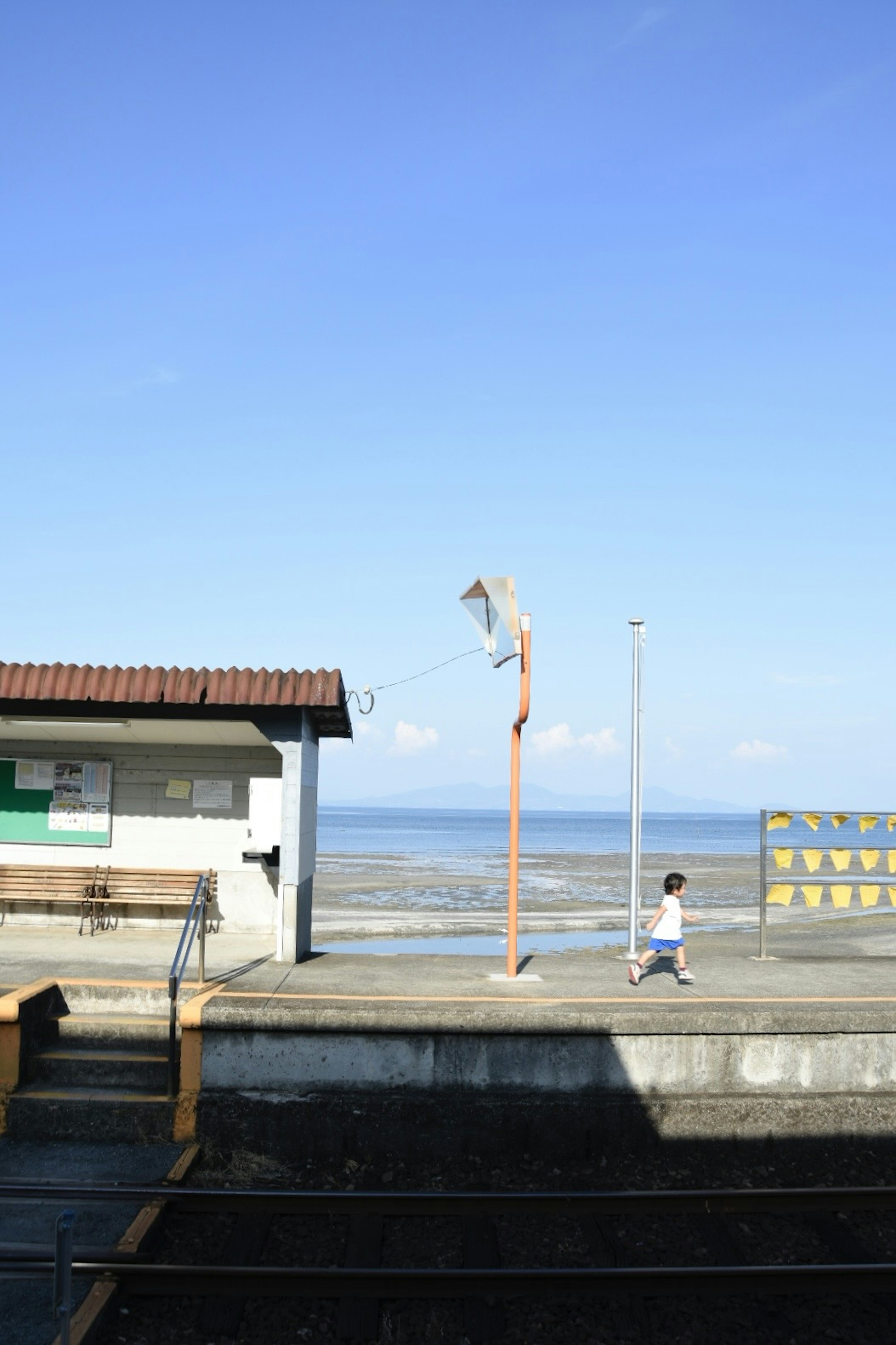 青空の下で海の近くを歩く子供と駅舎の風景