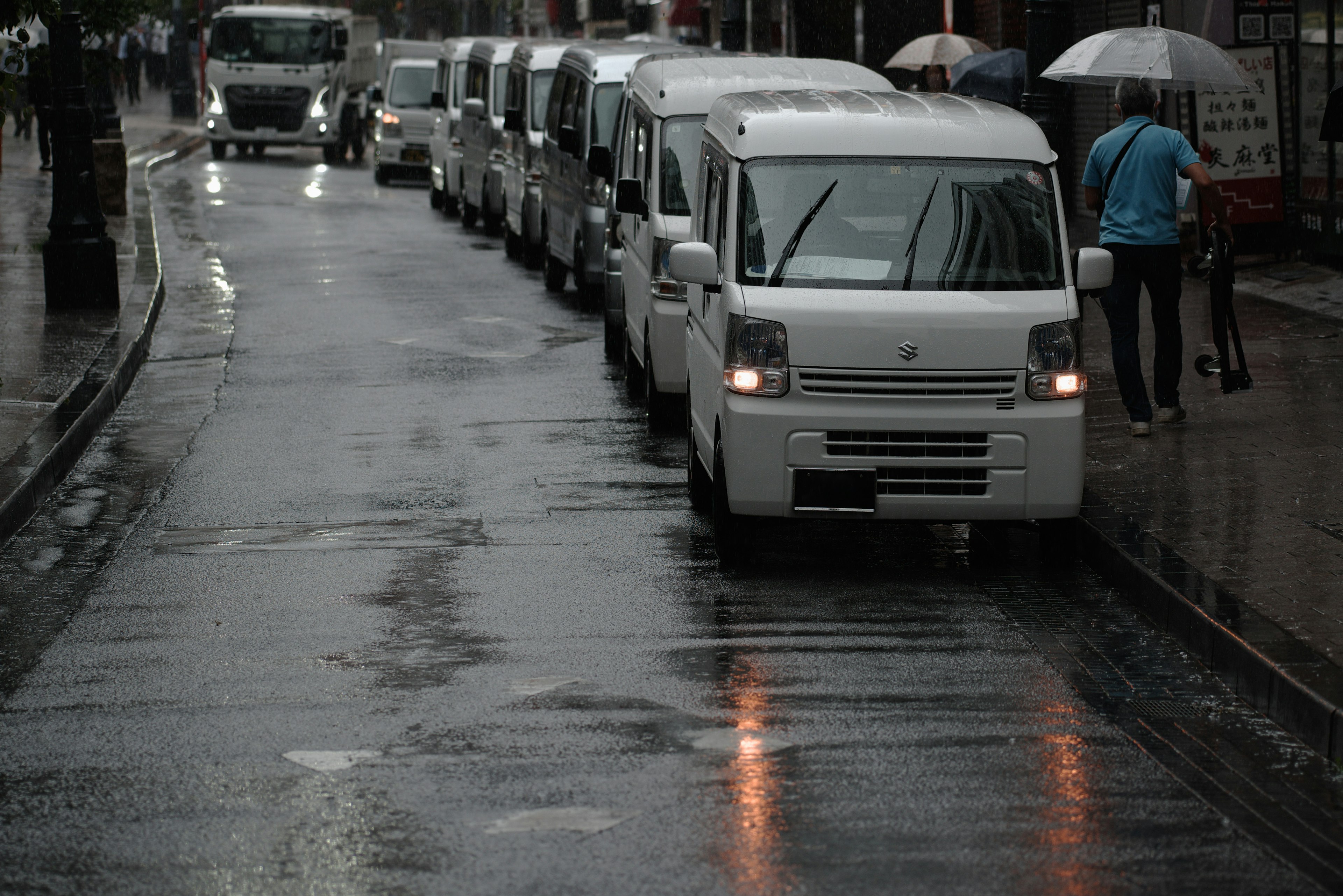 Reihe von weißen Kleintransportern auf einer regnerischen Straße mit einer Person mit einem Regenschirm