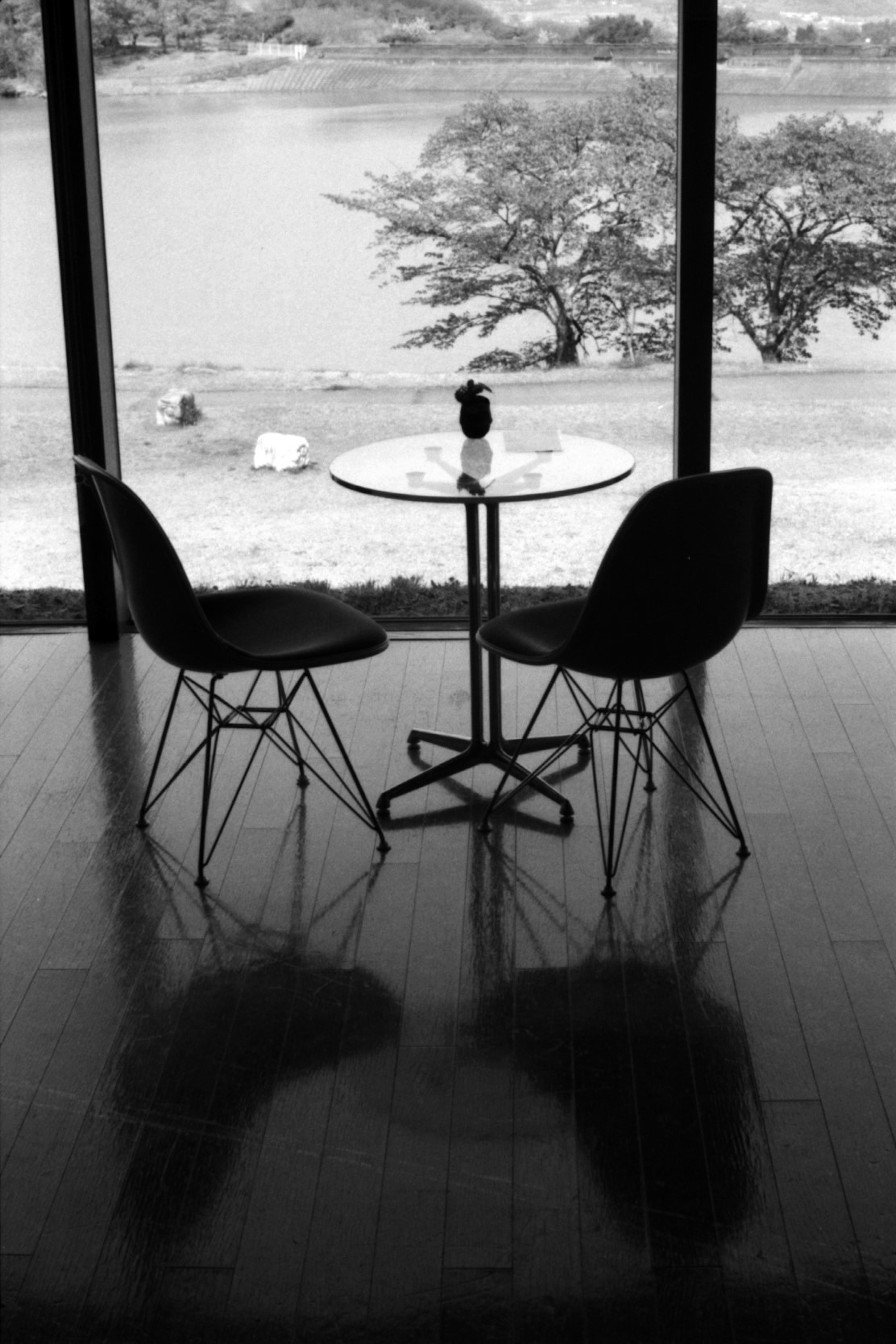 Photo en noir et blanc d'une table et de deux chaises près d'une fenêtre avec des ombres visibles