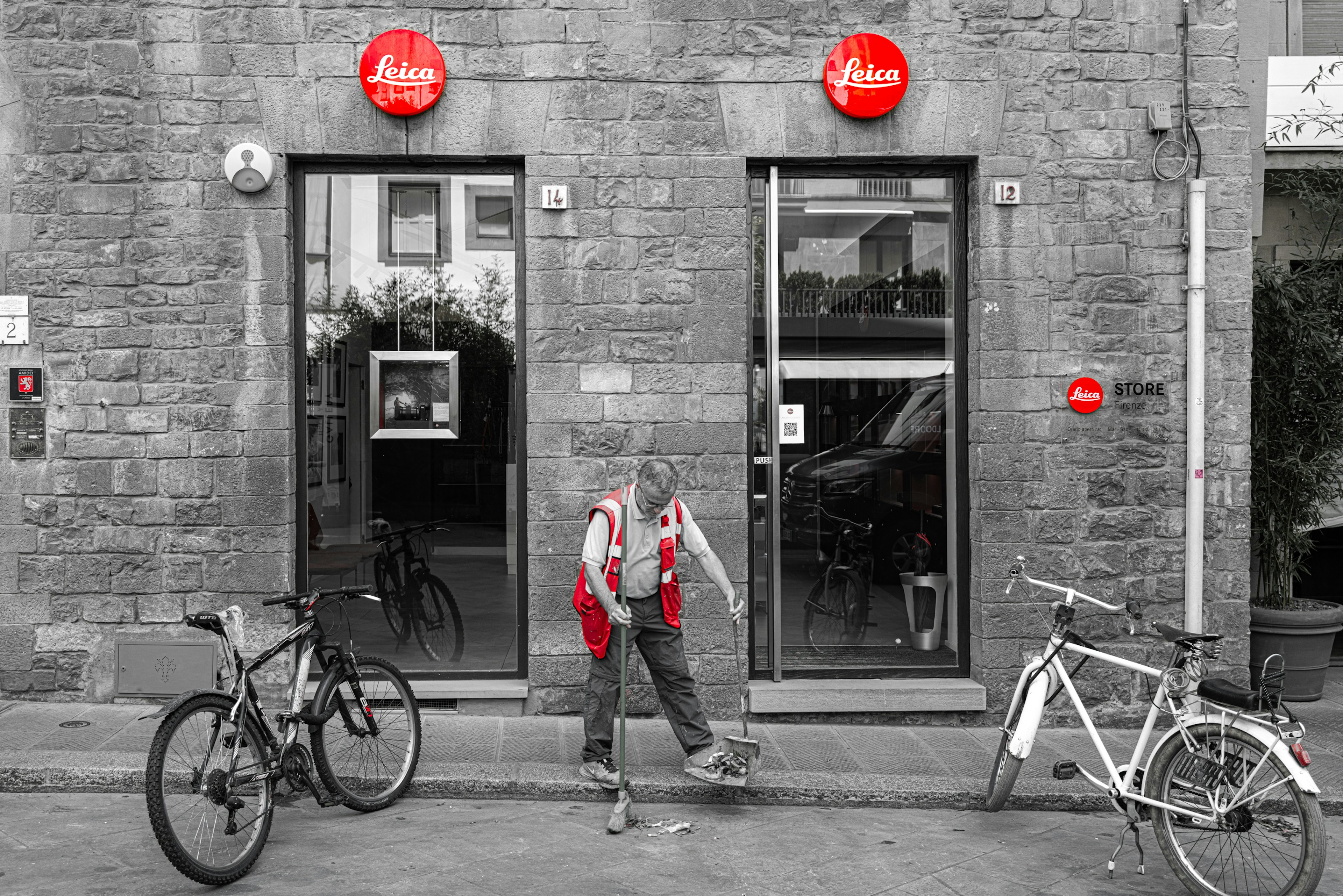 Donna in grembiule rosso che spazza vicino a biciclette davanti a un negozio con insegna rossa