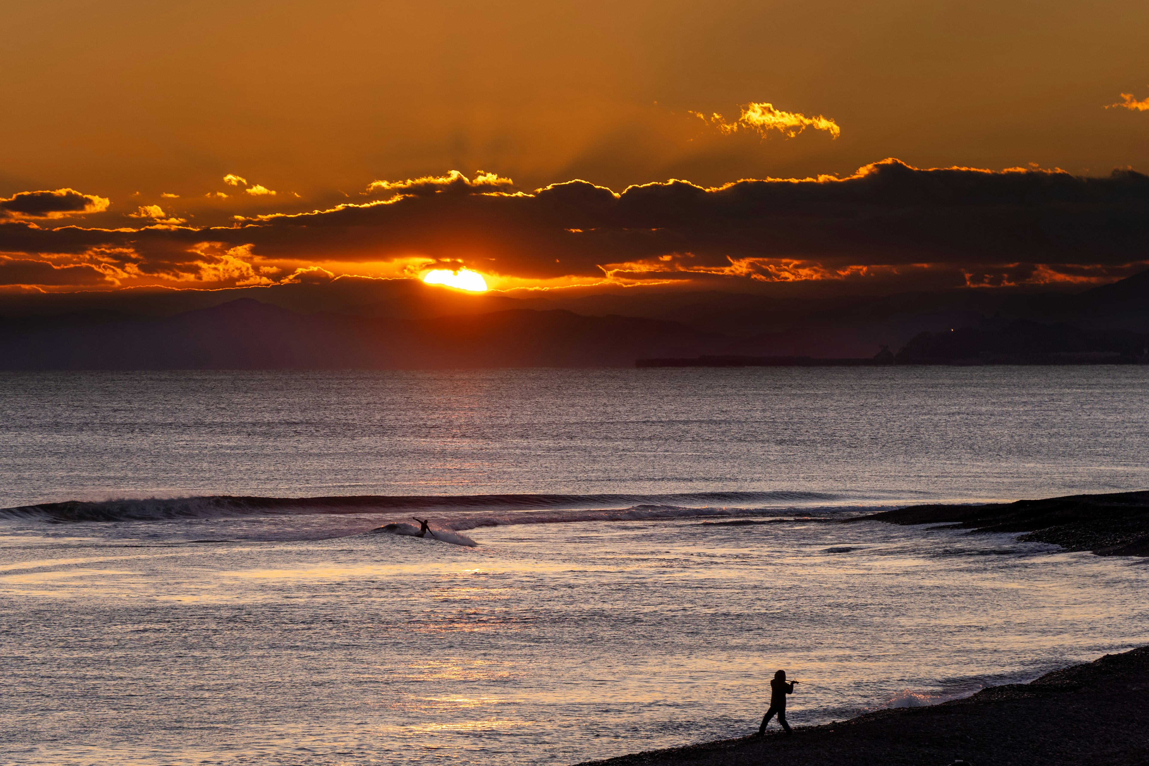 夕日が海に沈むビーチの風景 人が海岸を歩いている