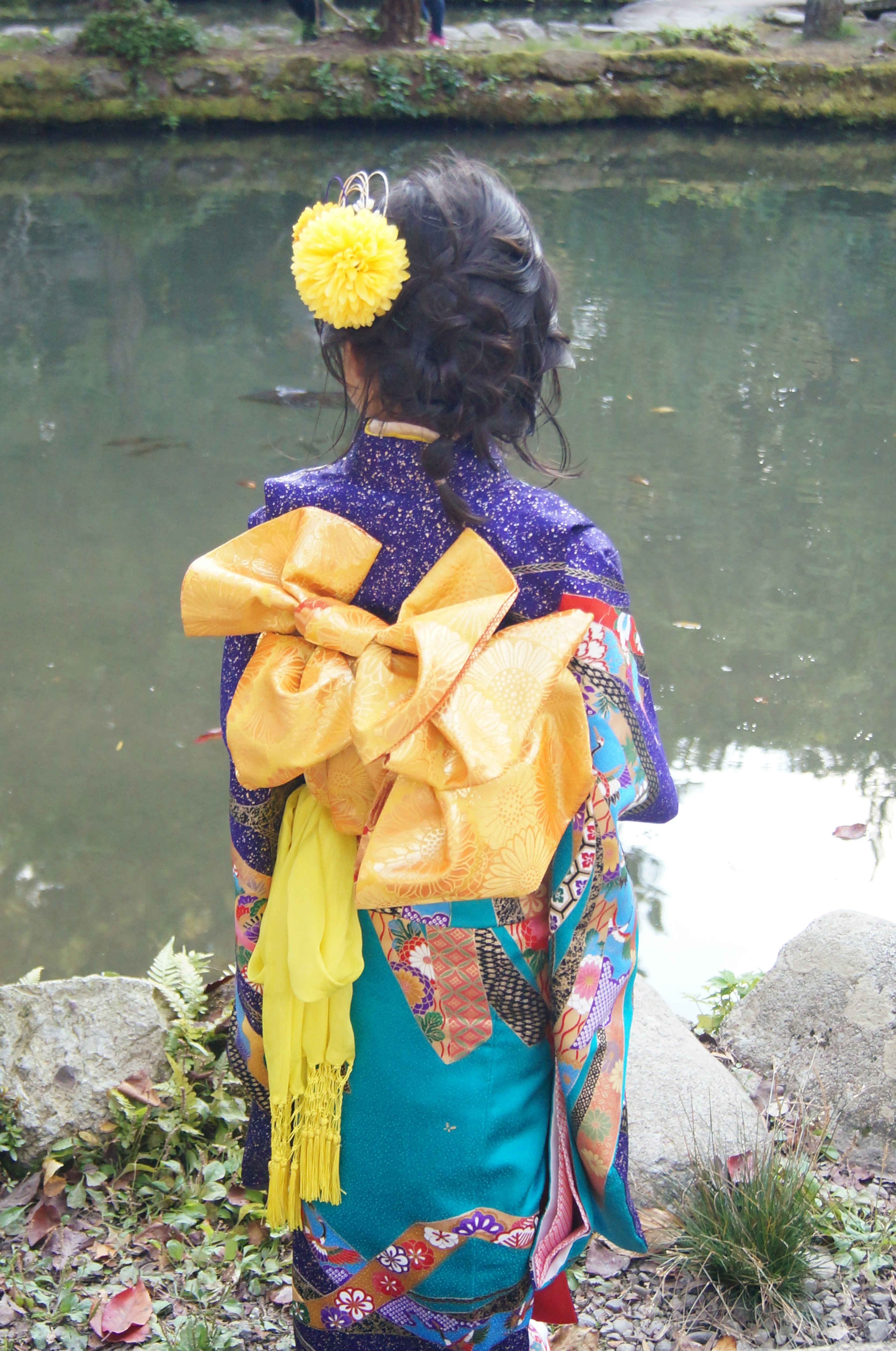 A child wearing a colorful kimono stands by a pond