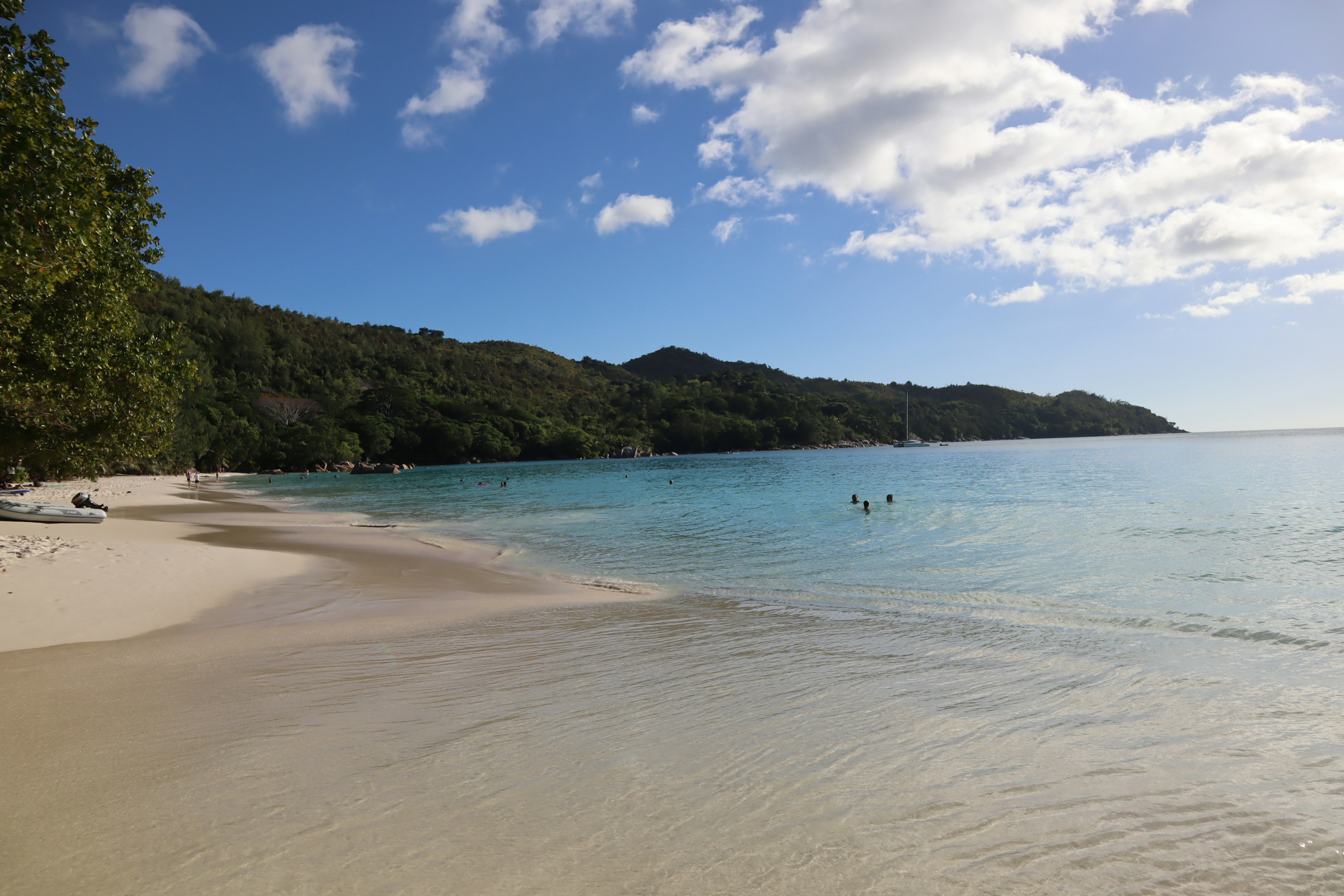 Scène de plage magnifique avec océan bleu et sable blanc, ciel ensoleillé, personnes nageant au loin