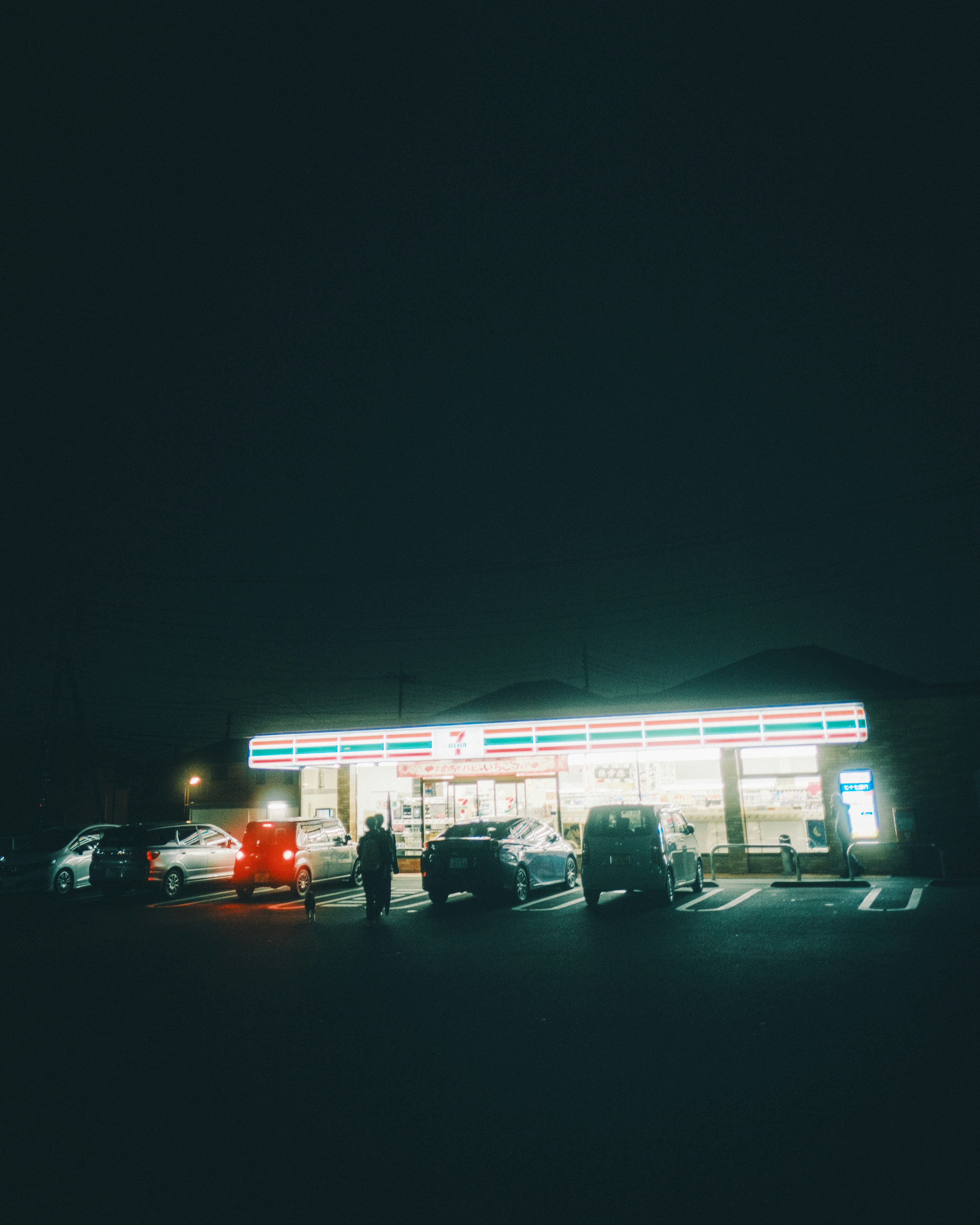 Exterior view of a convenience store at night with parked cars