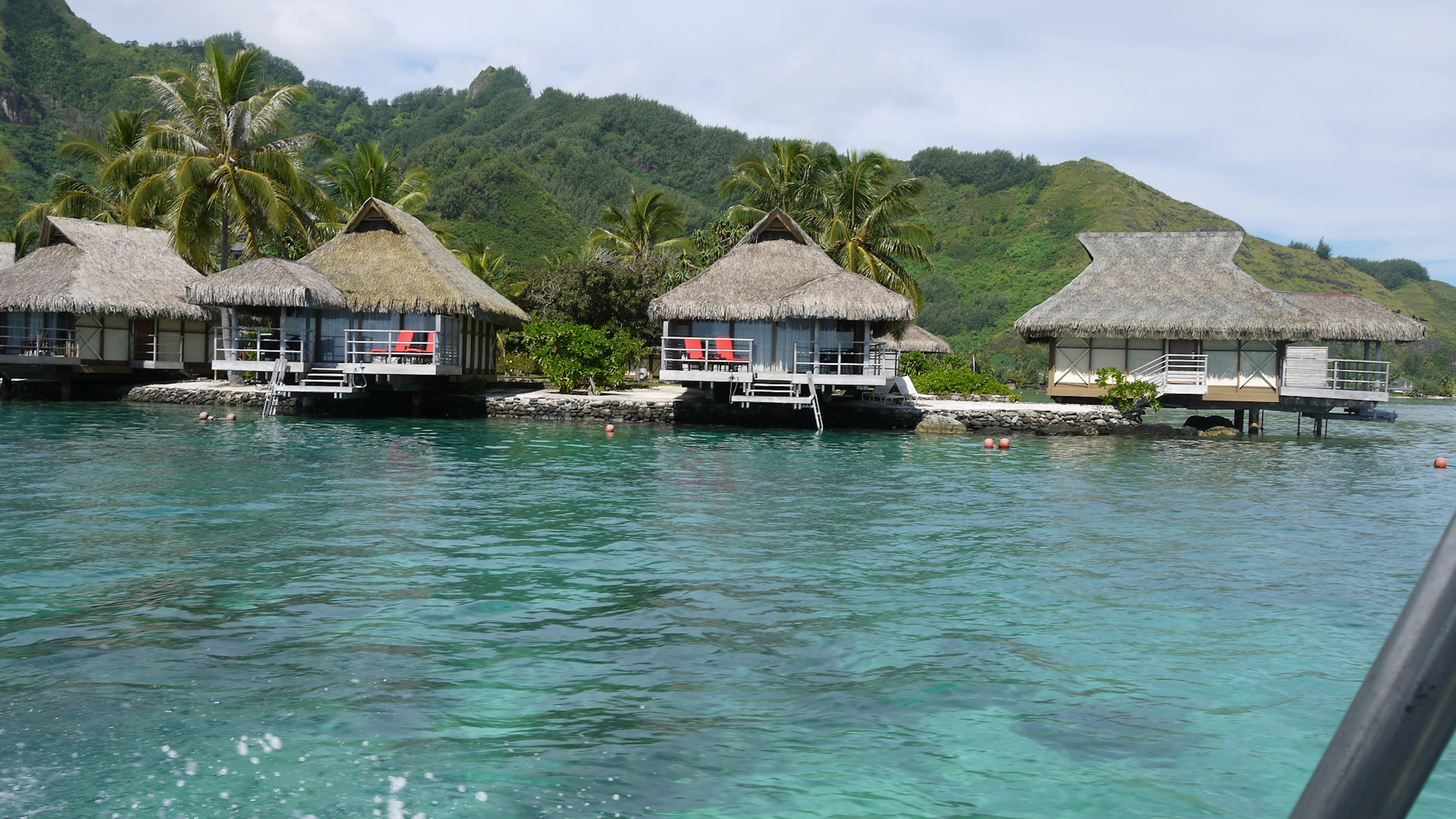 Bungalows on clear blue water surrounded by lush green mountains