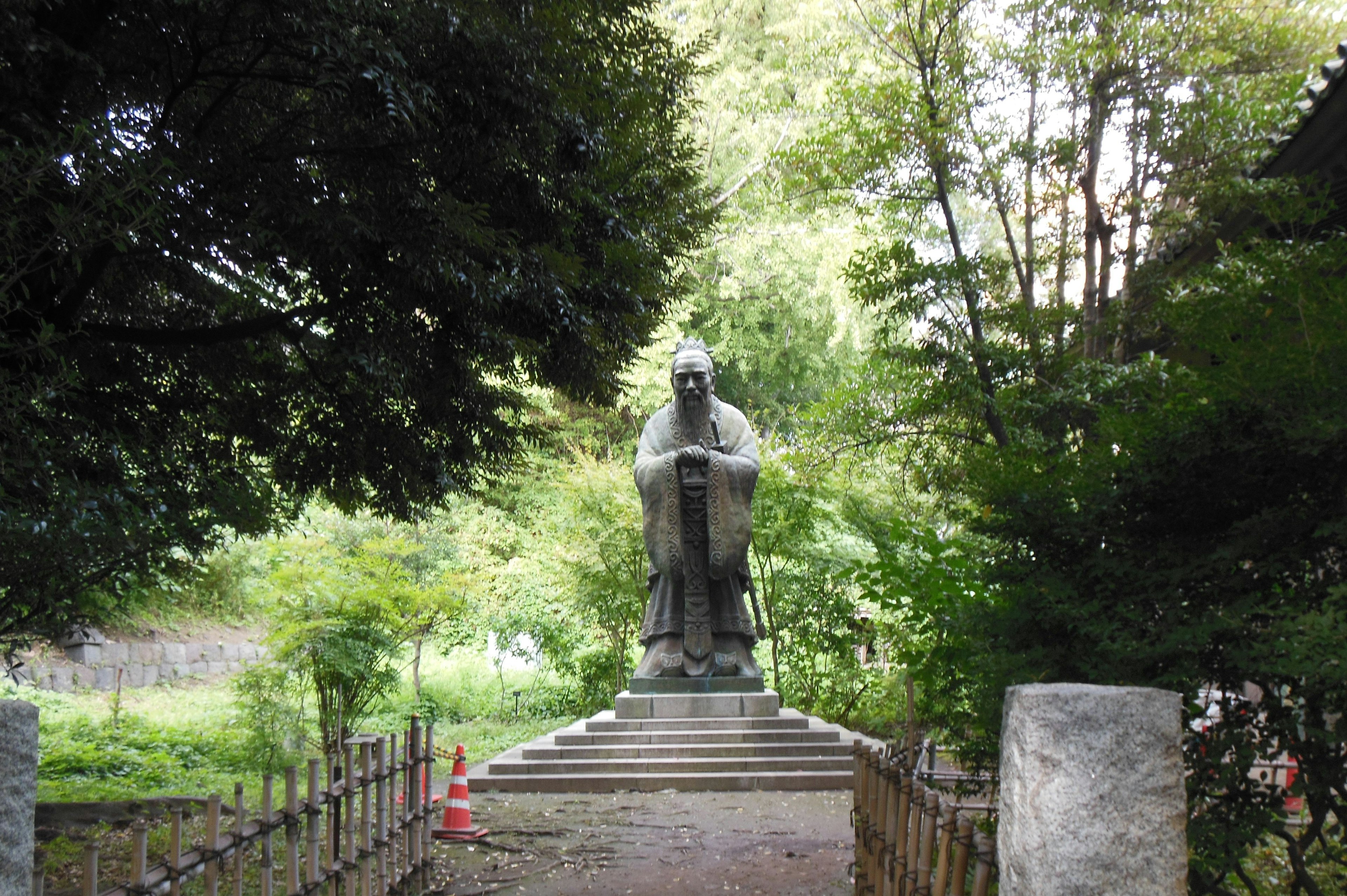 A large statue stands in a lush green environment along a quiet path