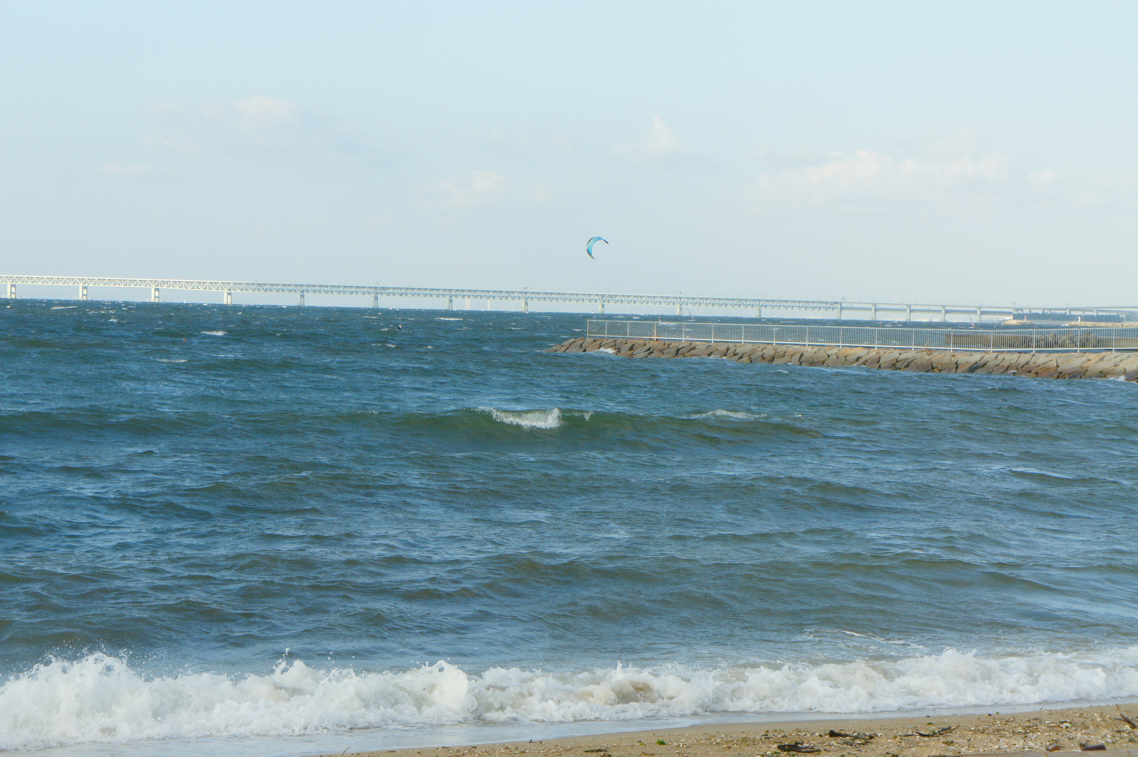 Blick auf das blaue Meer mit Wellen und Sandstrand entfernte Brücke im Hintergrund