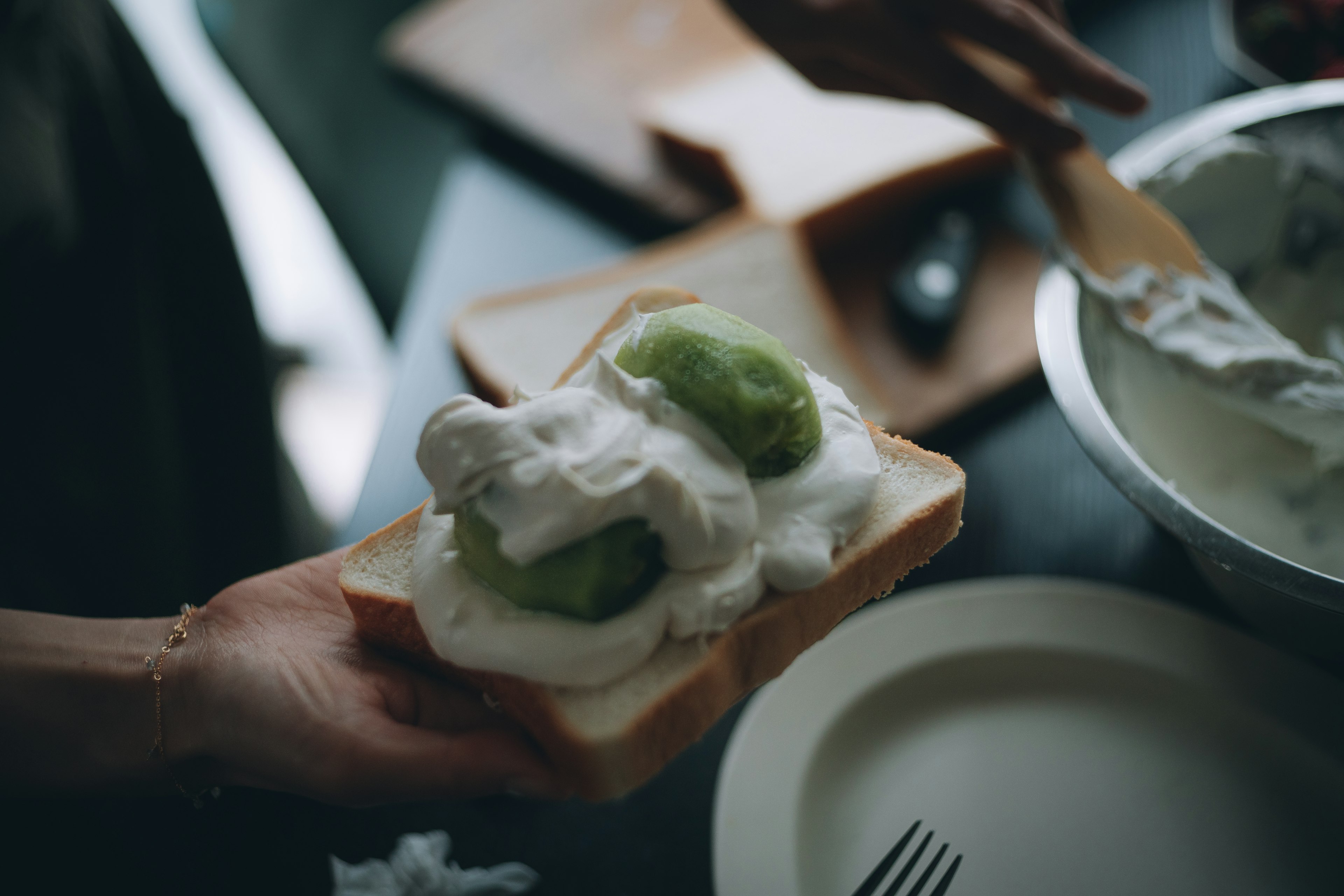 A slice of bread topped with cream and fruit held in a hand