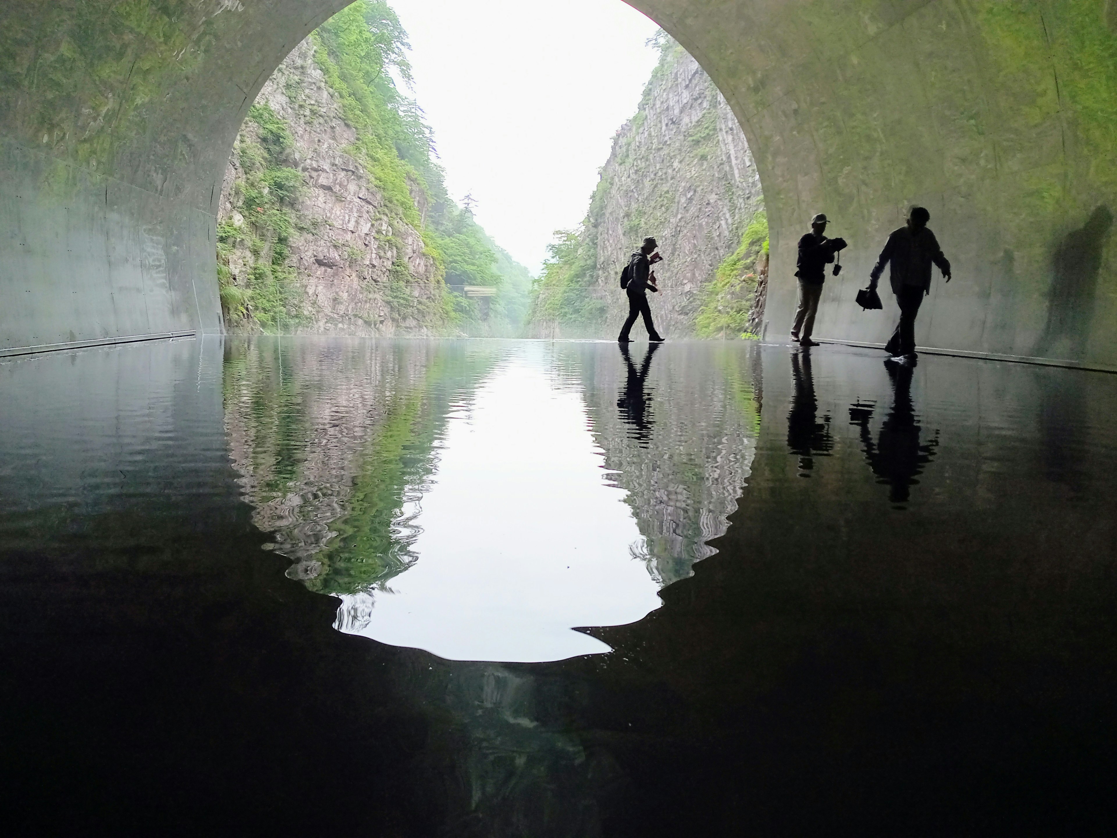 Silhouettes of people walking inside a tunnel with water reflection