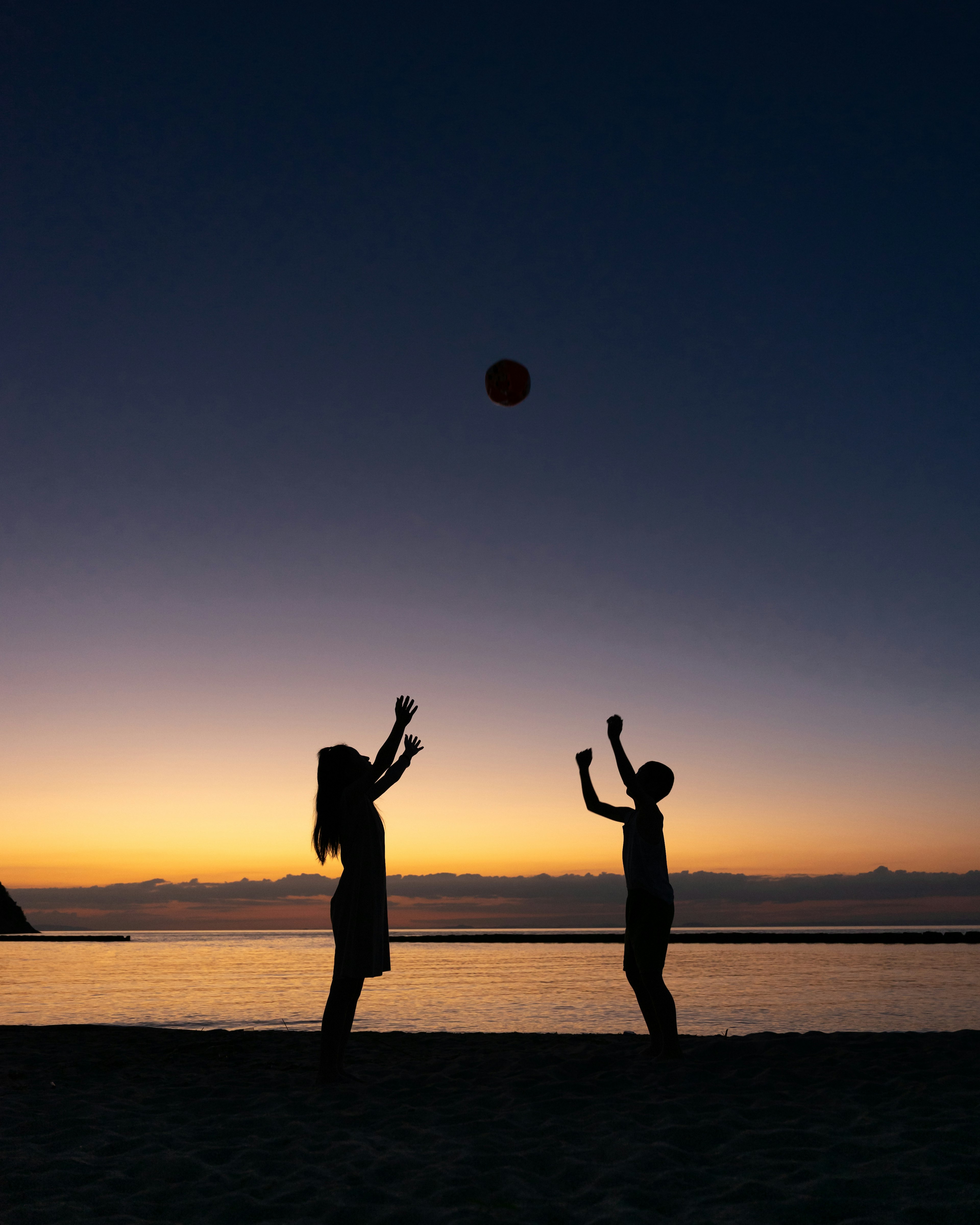 Siluet anak-anak bermain bola saat matahari terbenam di tepi laut