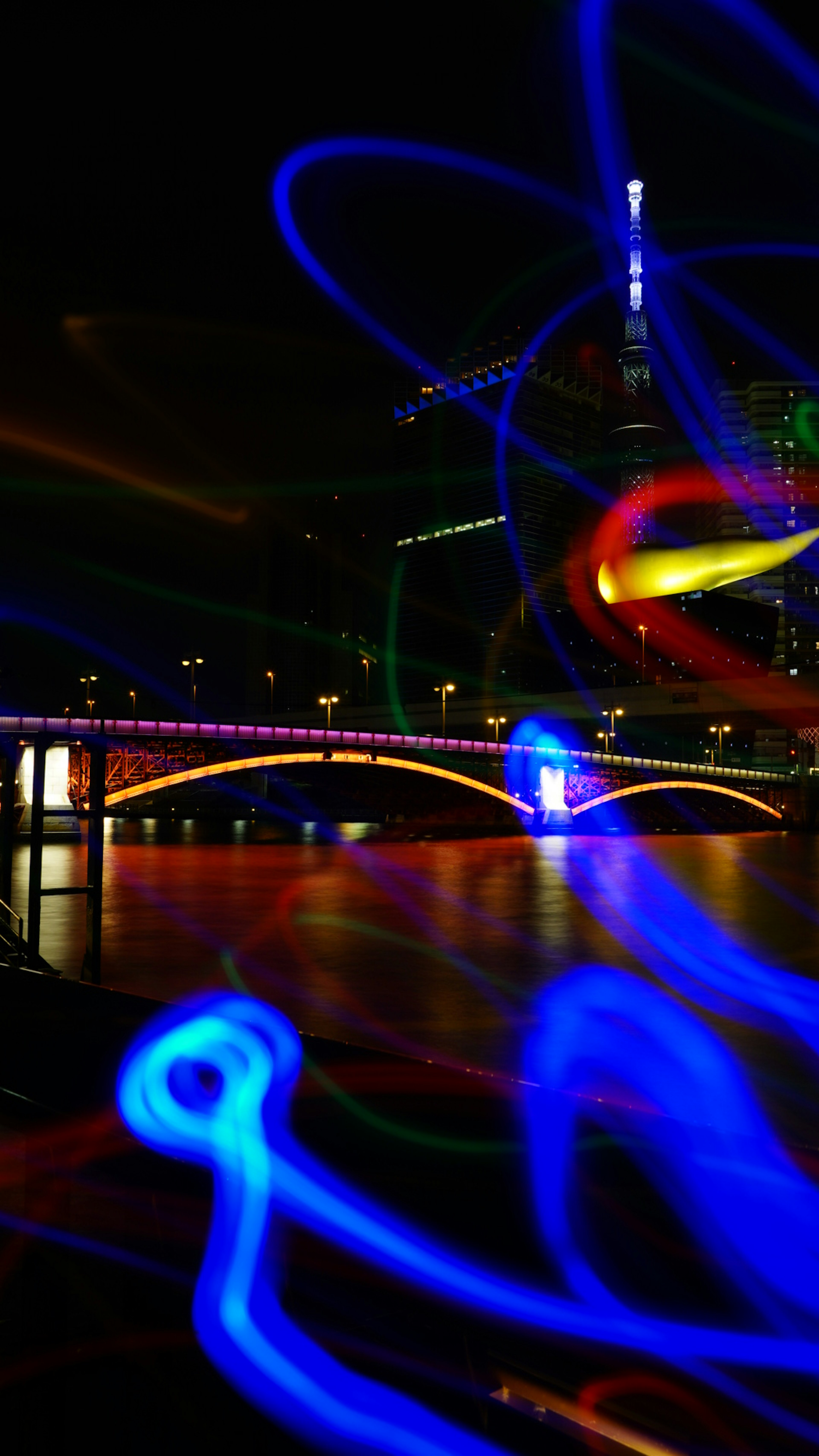 Colorful light trails over a bridge and reflections on the water in a night cityscape