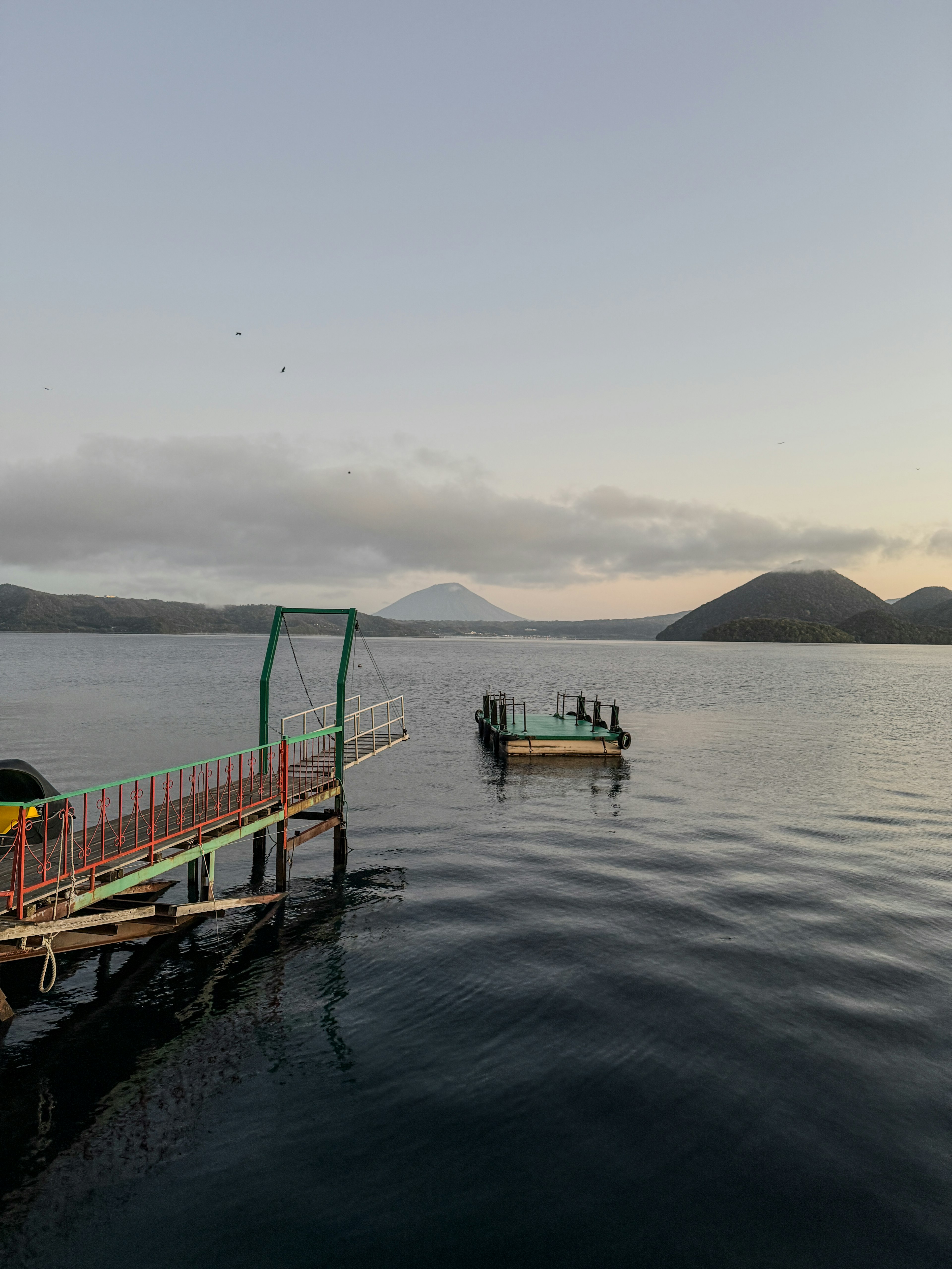 Ein ruhiger See mit einem kleinen Steg und Bergen im Hintergrund