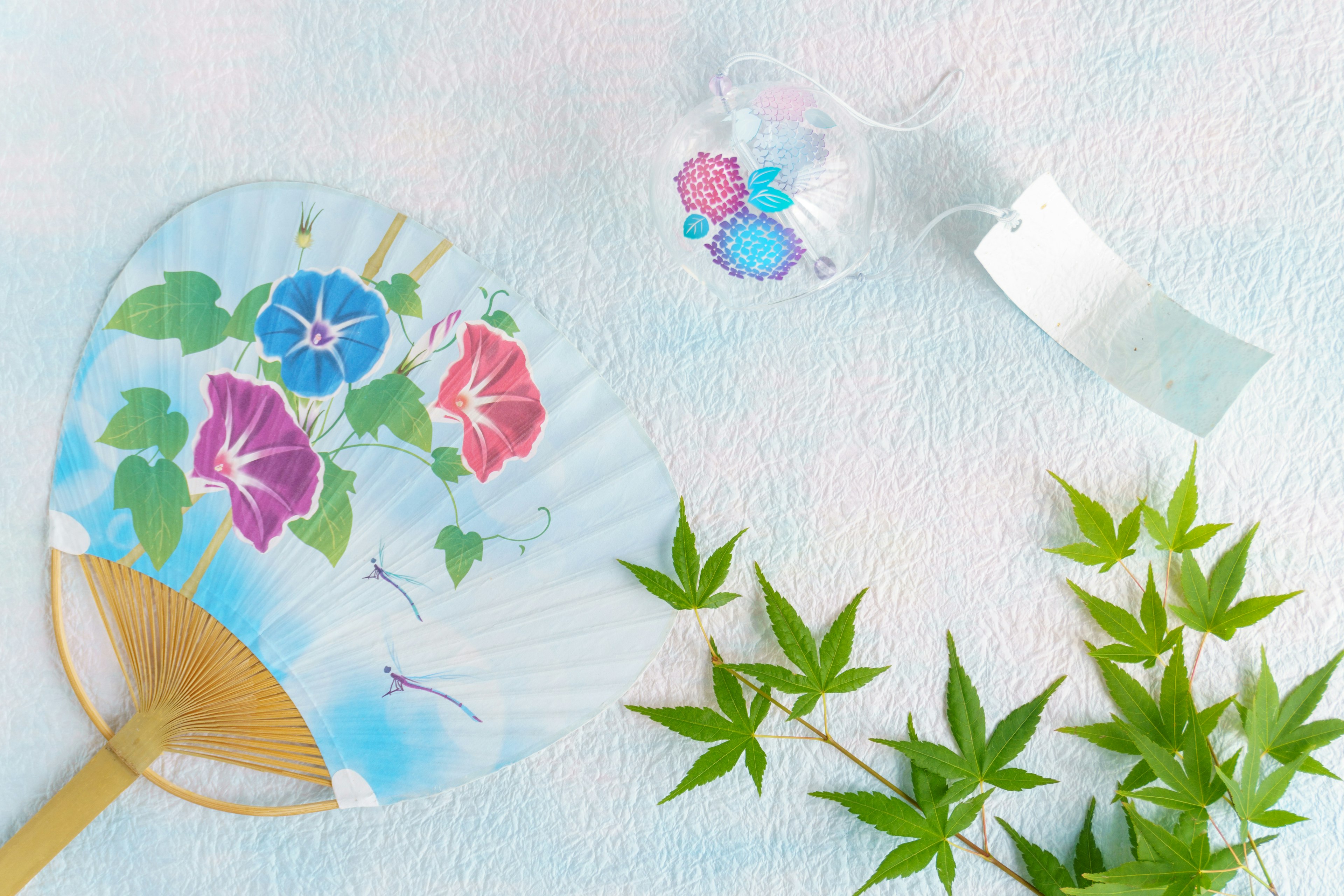 Collage of a fan with morning glory design and green leaves on a blue background