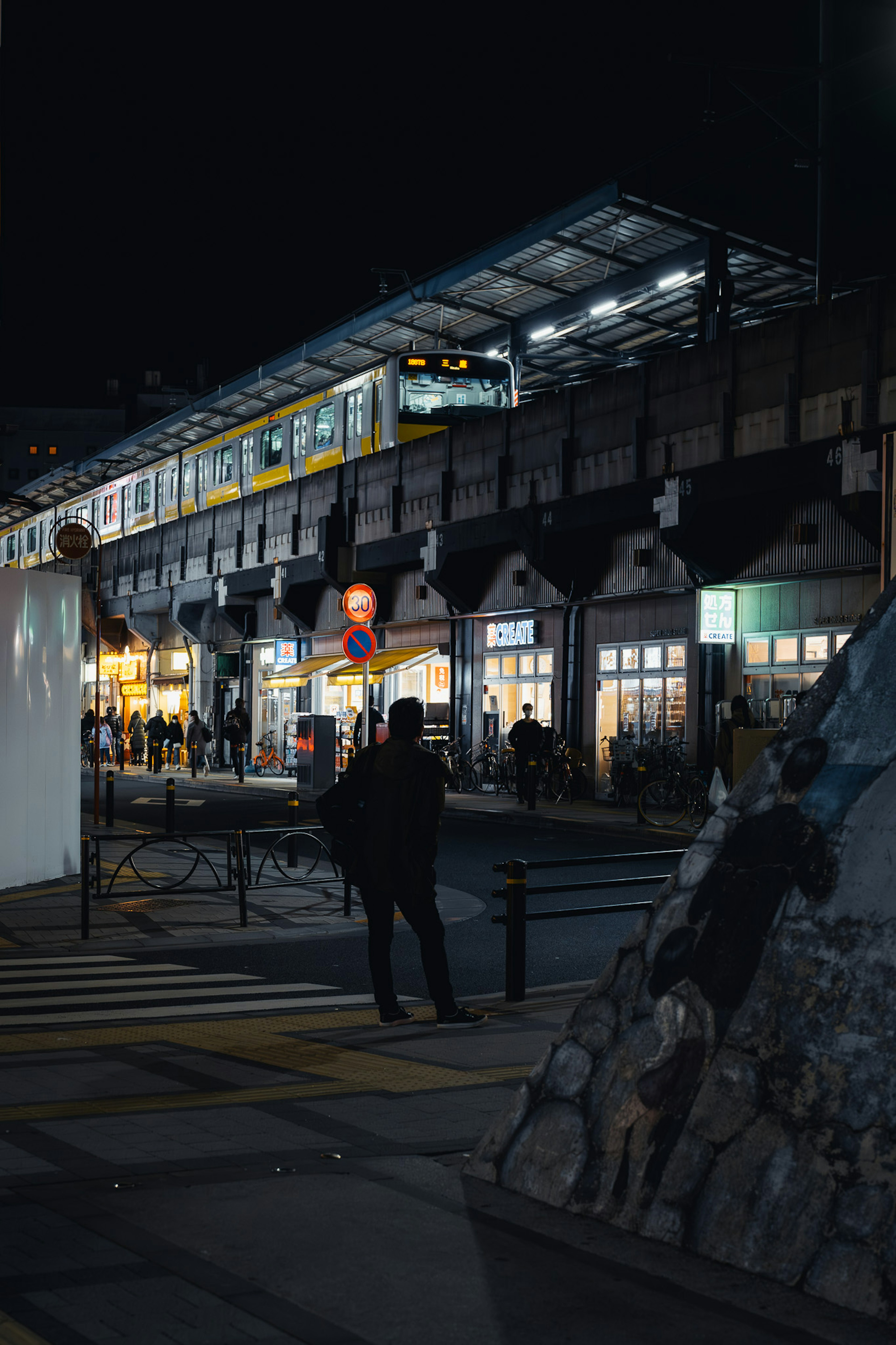 夜の街並みに立つ人と明るい店舗のある駅