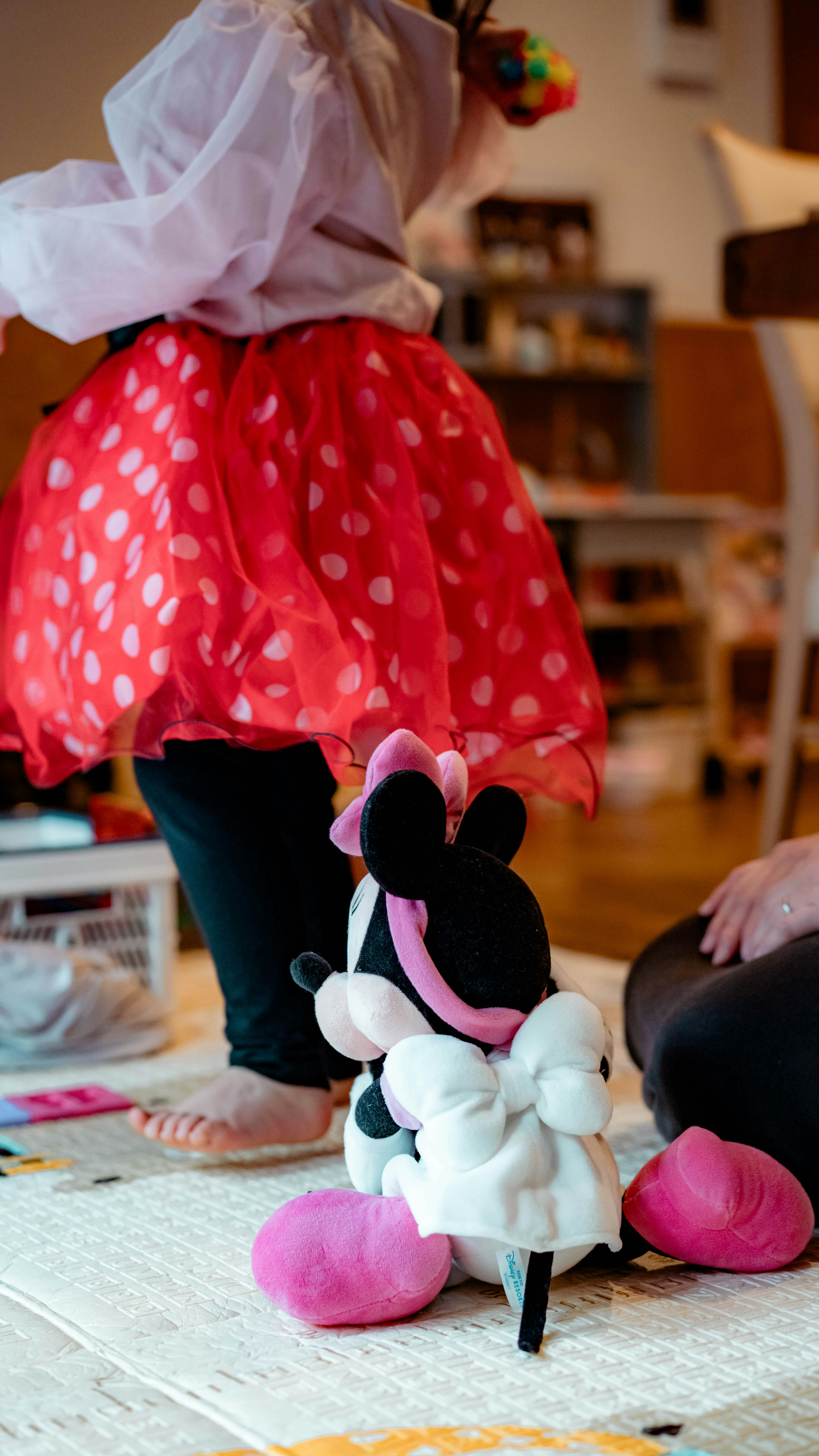 A child playing near a Minnie Mouse plush toy wearing a red polka dot skirt