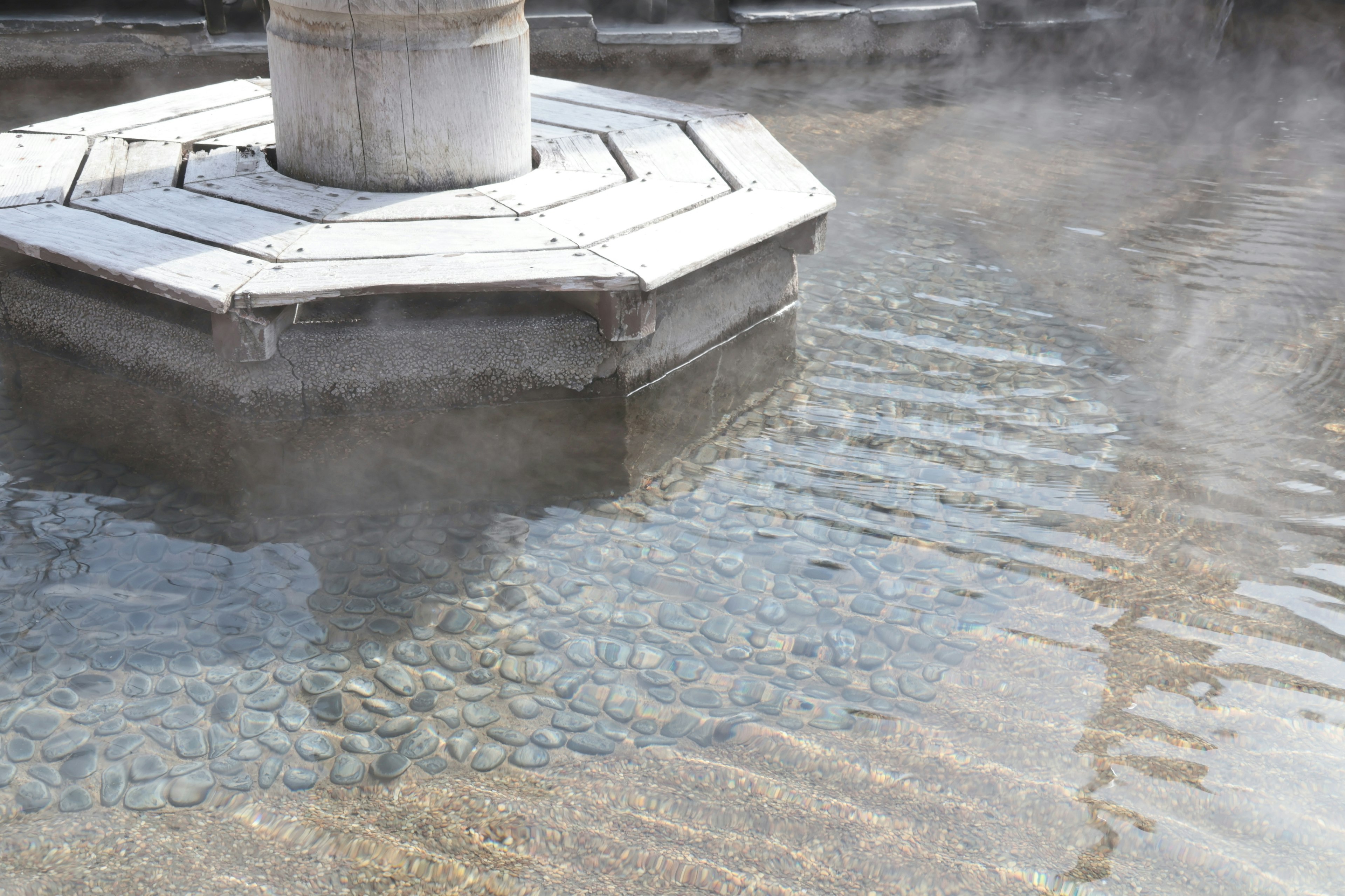 Octagonal structure with a stone base and steam rising from the hot spring water