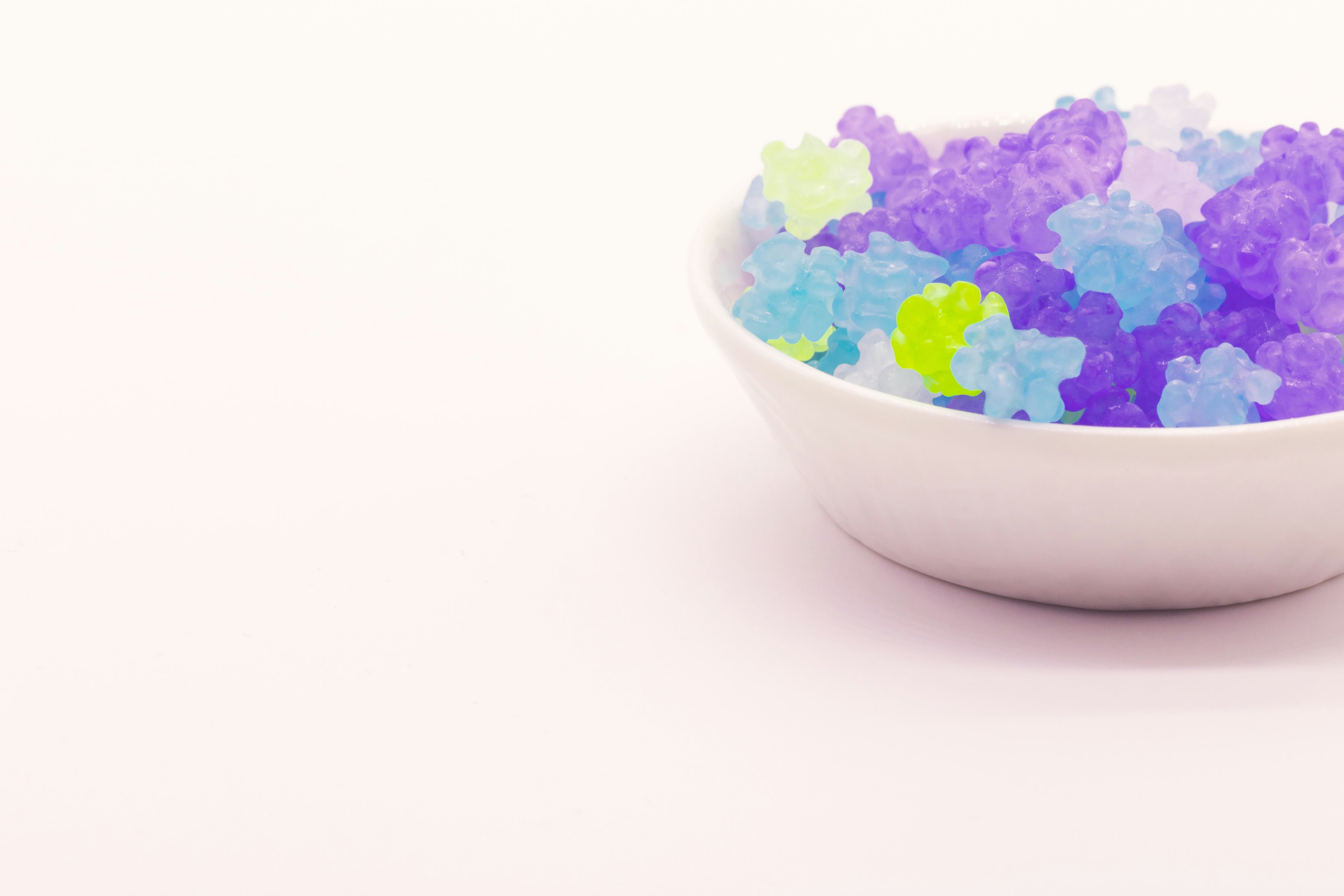 A white bowl filled with colorful ice-like crystals on a white background