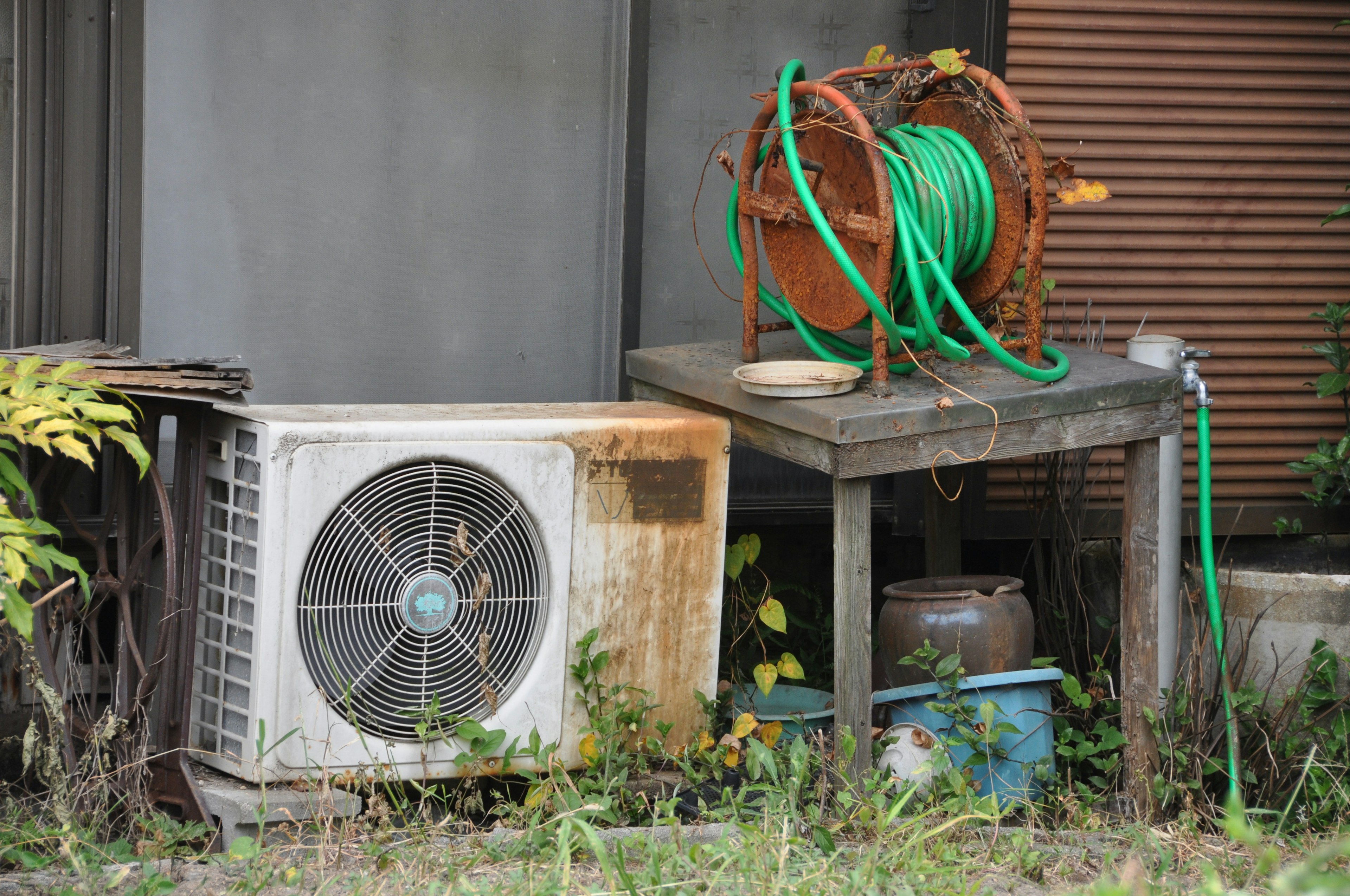 Old air conditioning unit next to a wooden table with a green hose