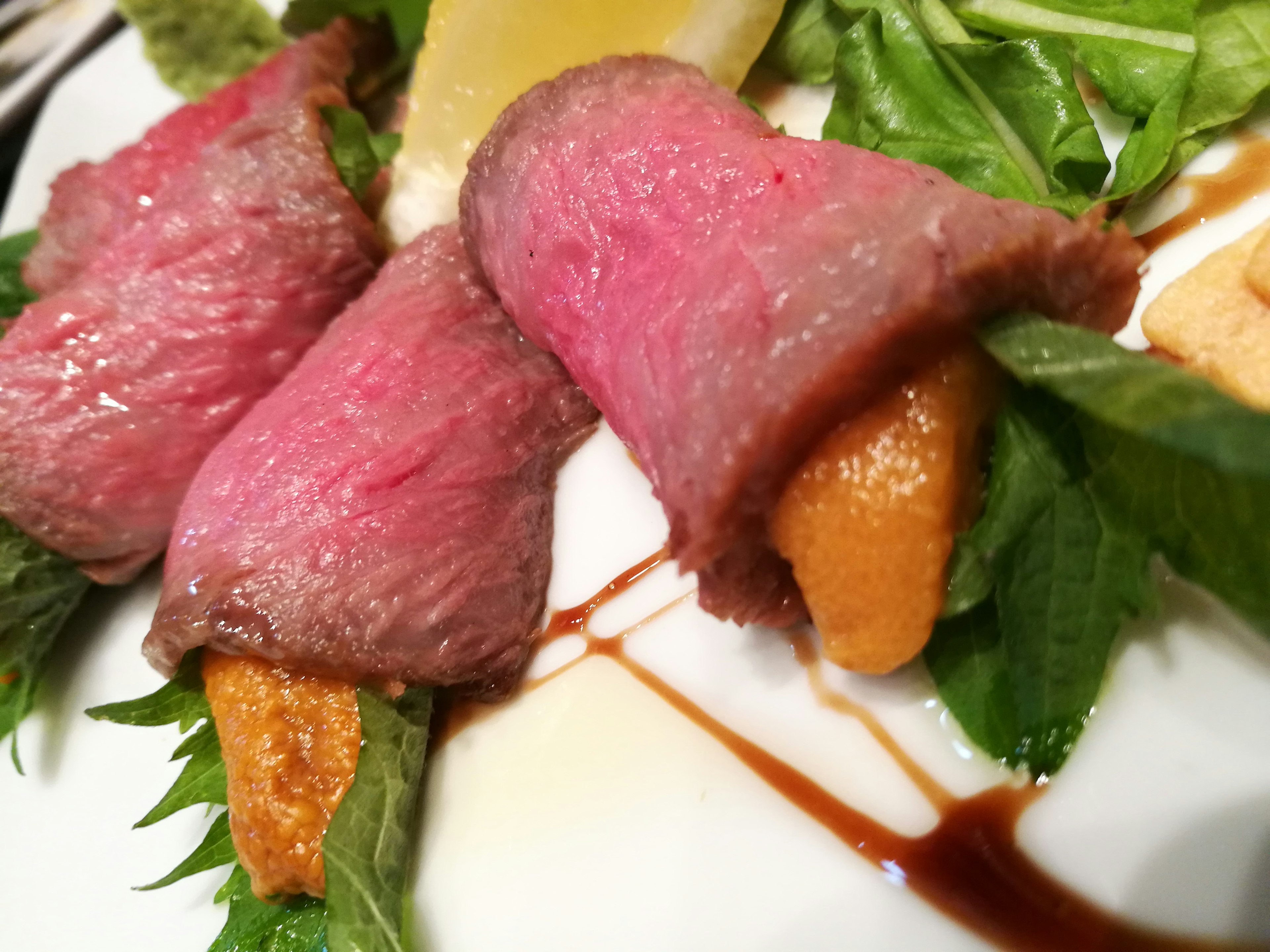 Carne de res en rodajas finas sobre una cama de verduras con acentos naranjas