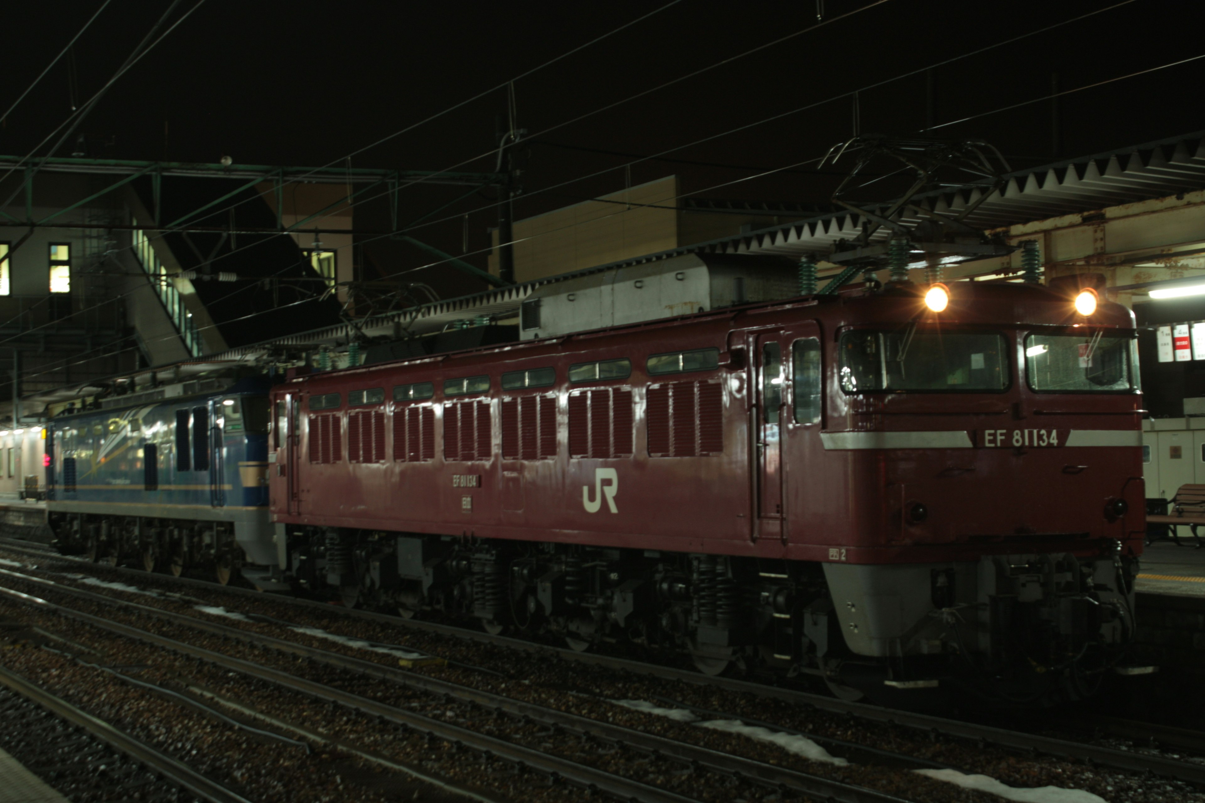 Red electric locomotive and blue train stopped at night station