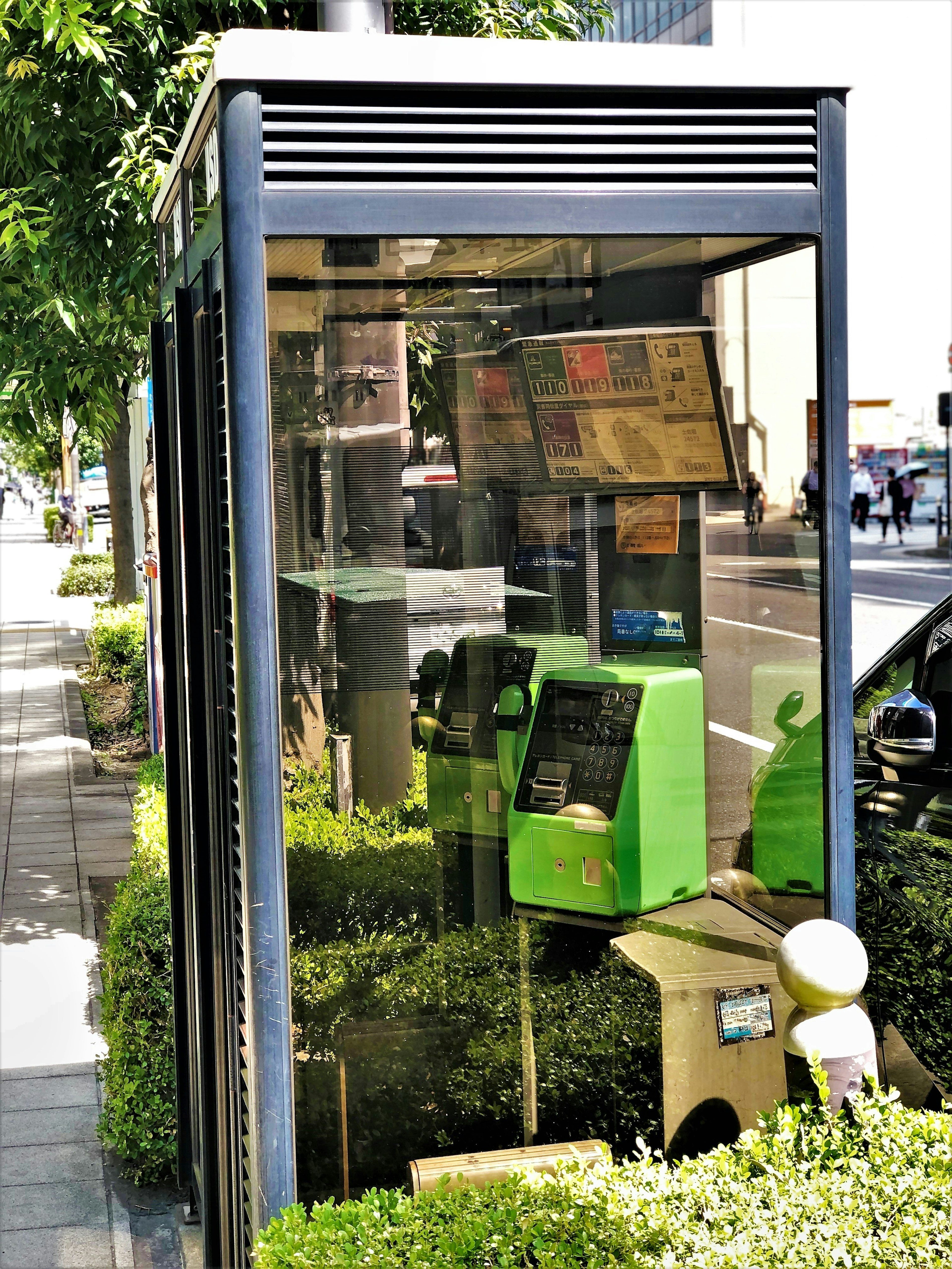 Transparent phone booth with a green public phone in an urban setting