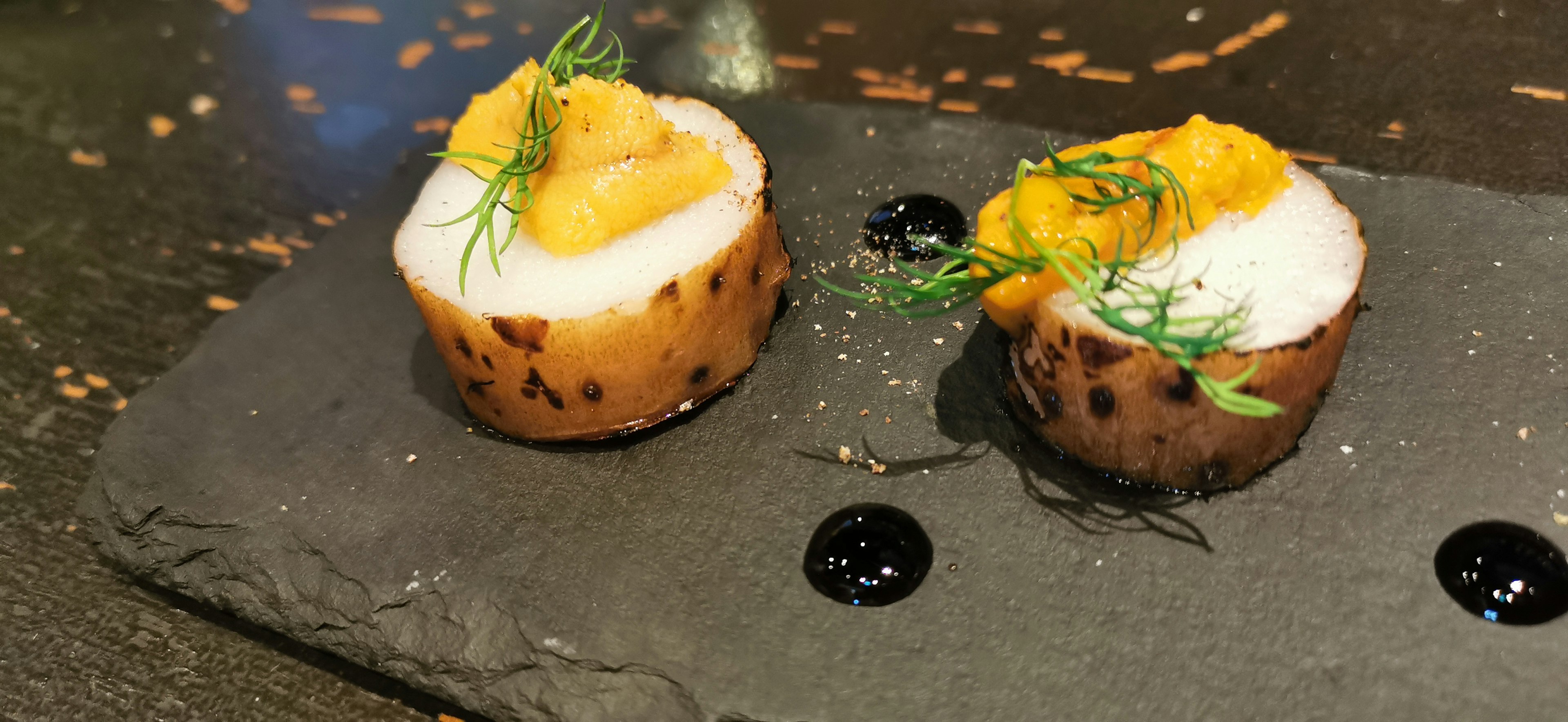 Dos platos similares a sushi presentados en un plato de piedra negra