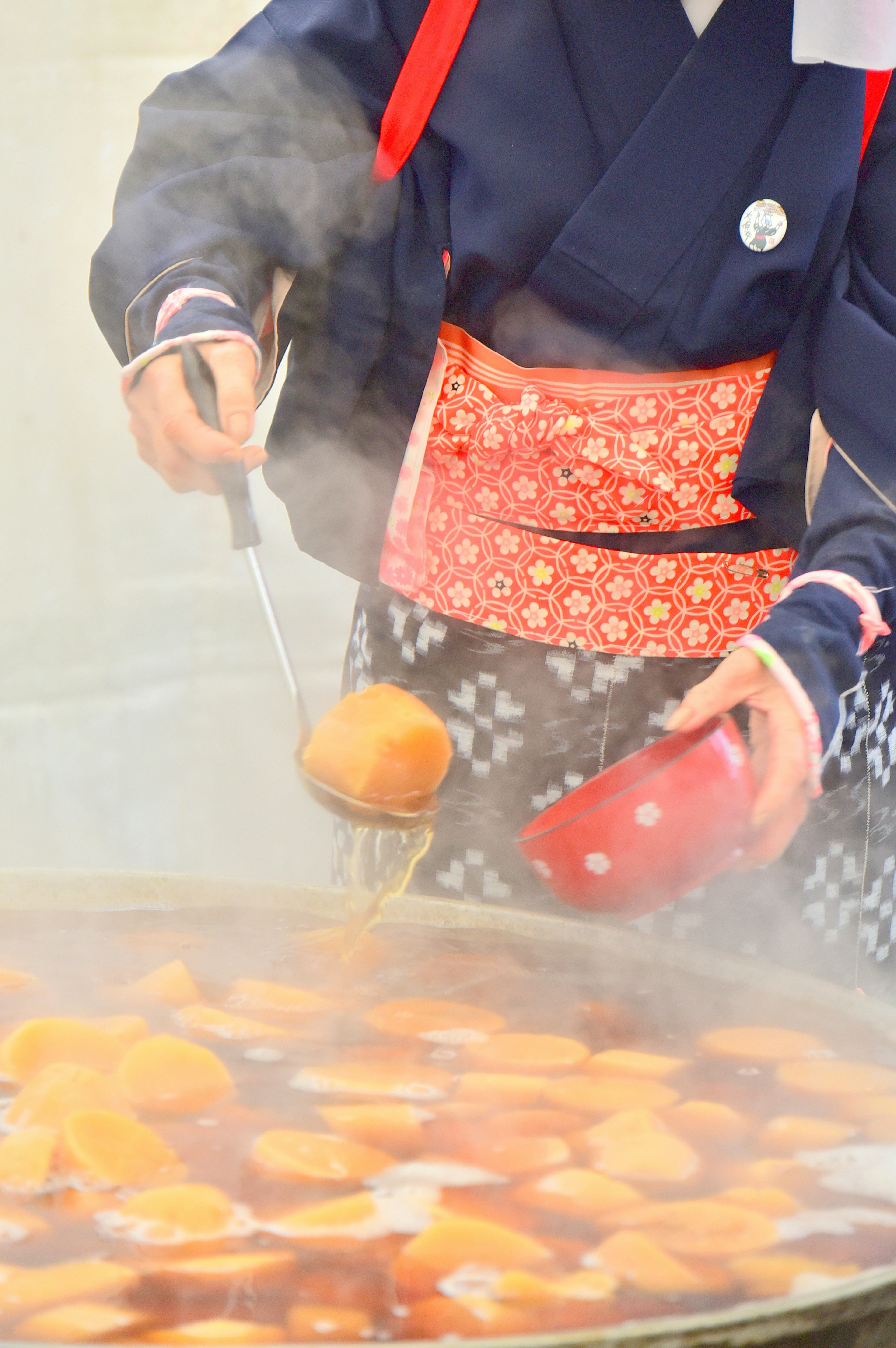 Seorang koki berpakaian tradisional menyiapkan makanan manis dalam uap