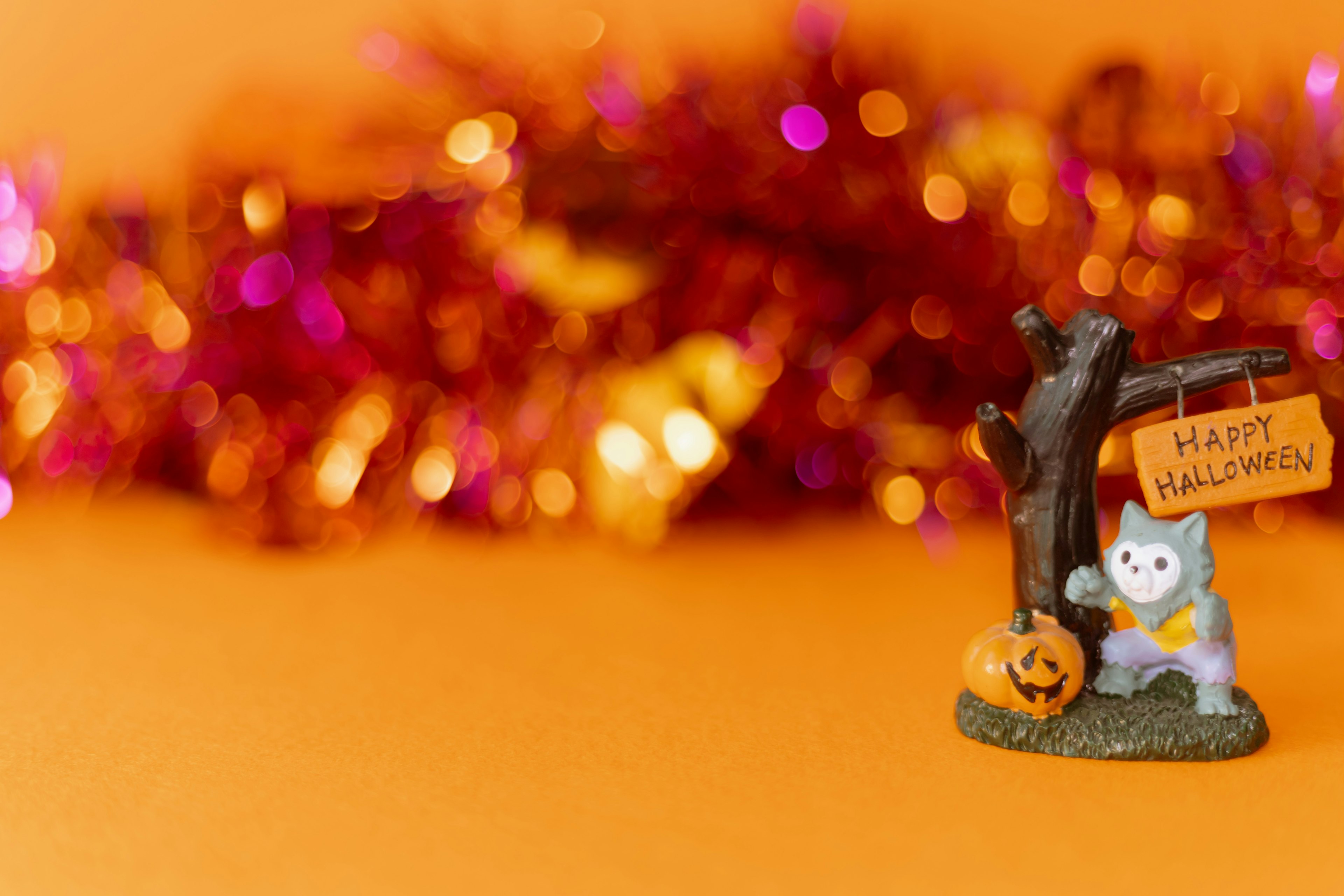 A Halloween decoration featuring a cat figurine next to a pumpkin on an orange background