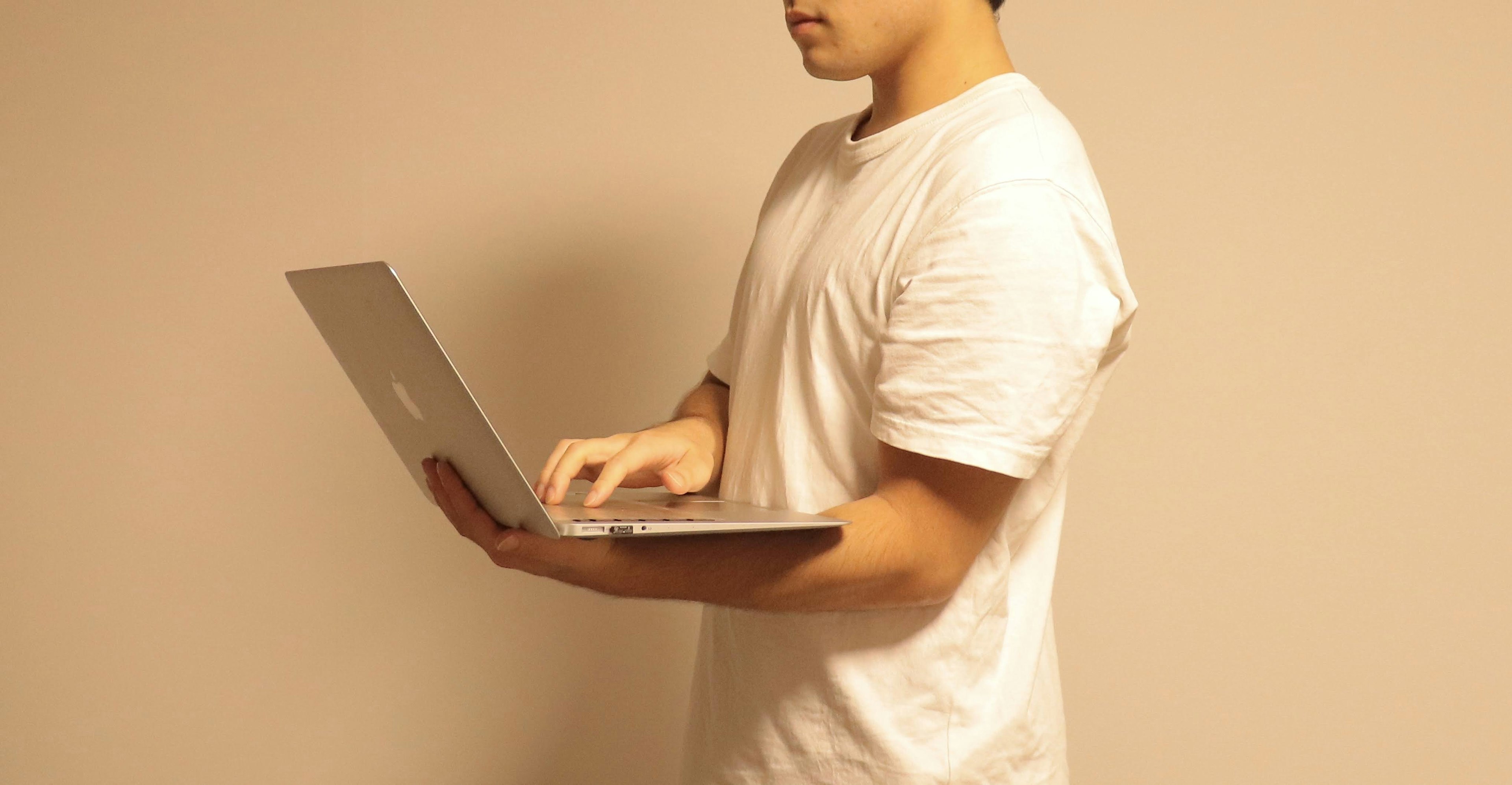 Un hombre con camiseta blanca sosteniendo una computadora portátil de pie