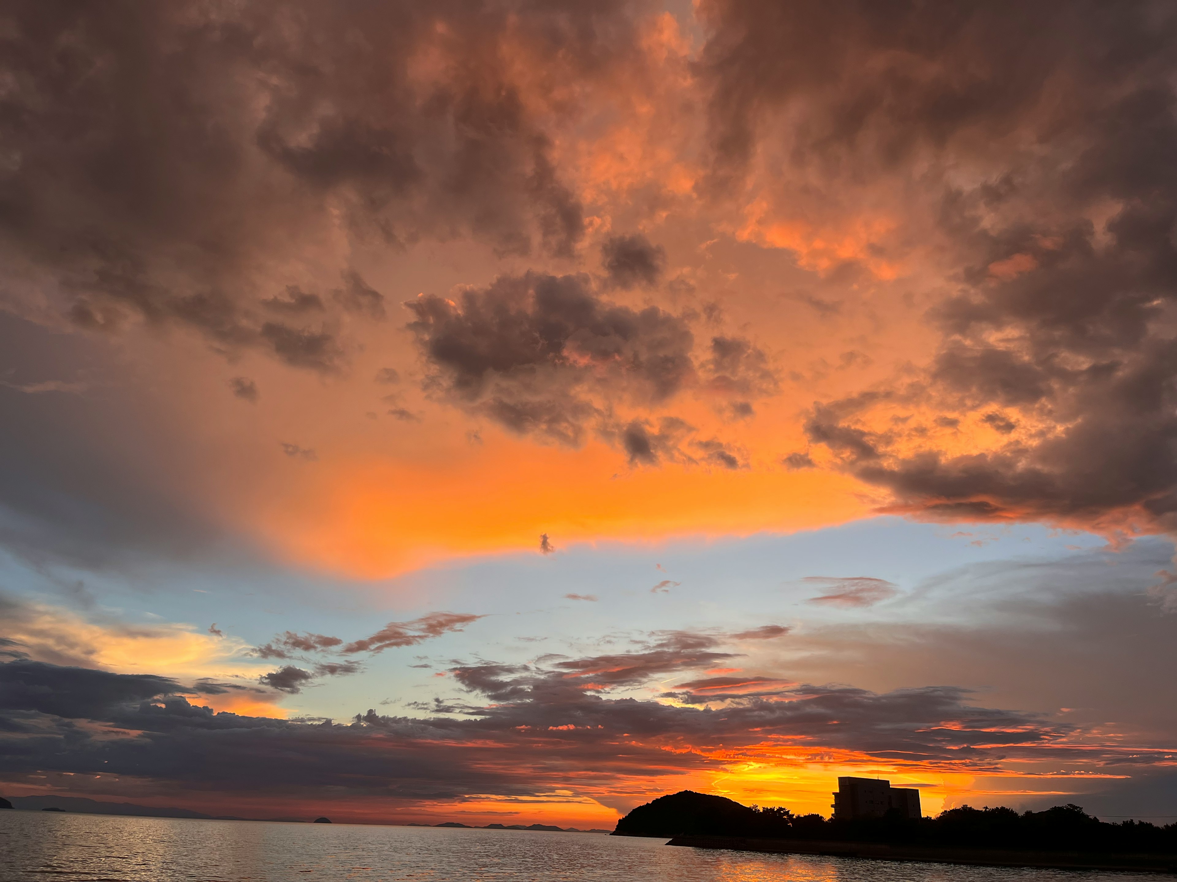 Bellissimo cielo al tramonto sopra il mare con nuvole arancioni e silhouette di un edificio