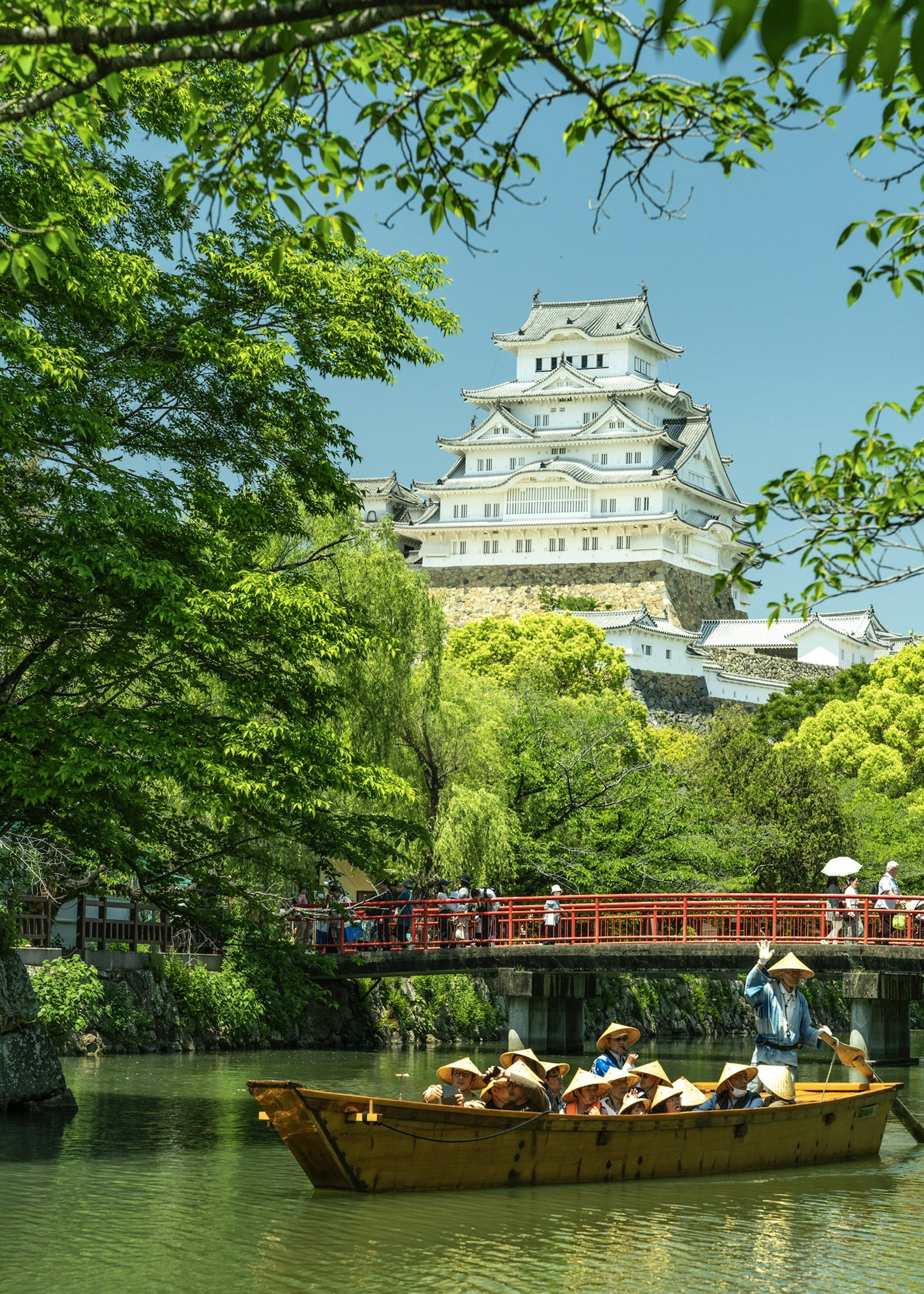 Kastil Himeji dikelilingi oleh pepohonan rimbun dengan orang-orang yang menikmati naik perahu