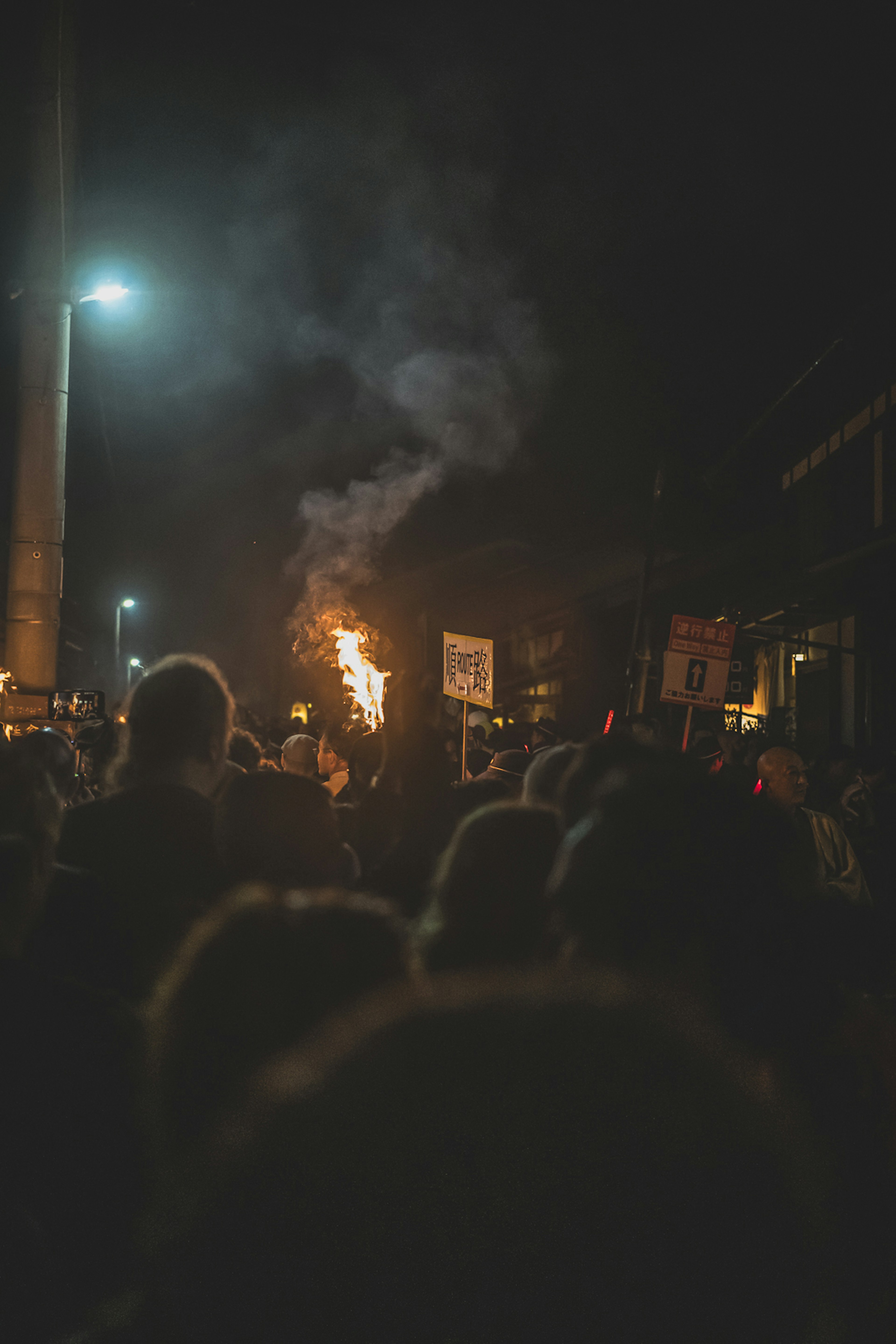 Crowd gathering at night with flames and smoke