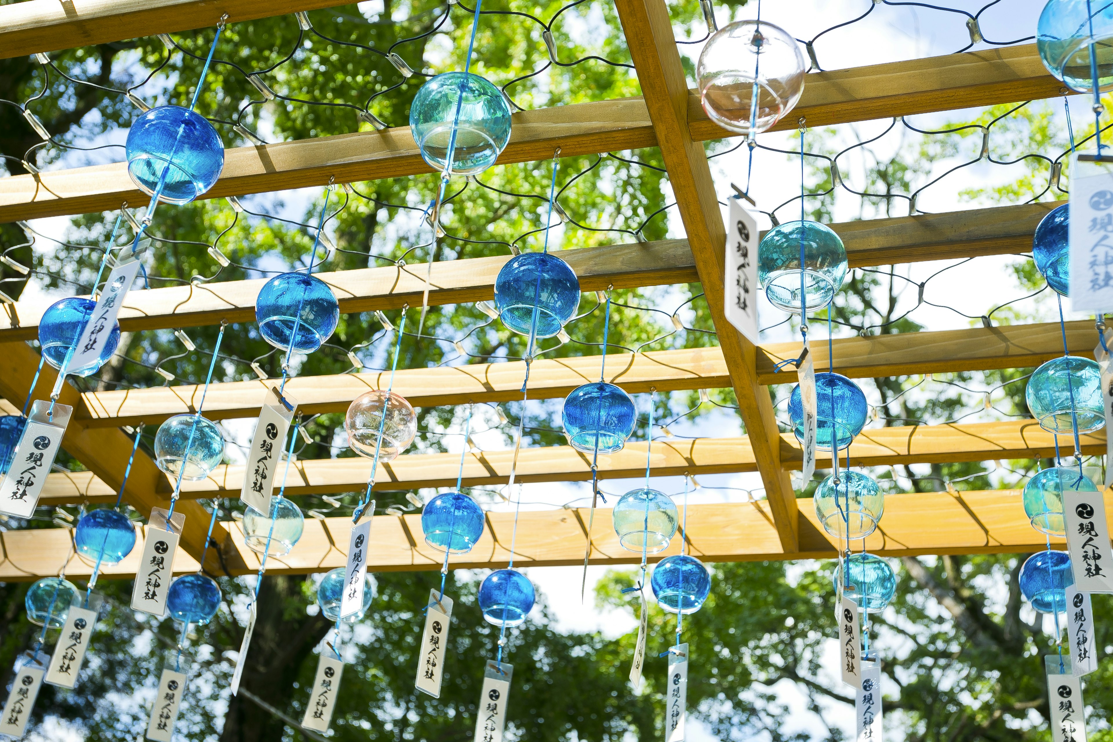 Blue wind chimes hanging from a wooden structure surrounded by green trees