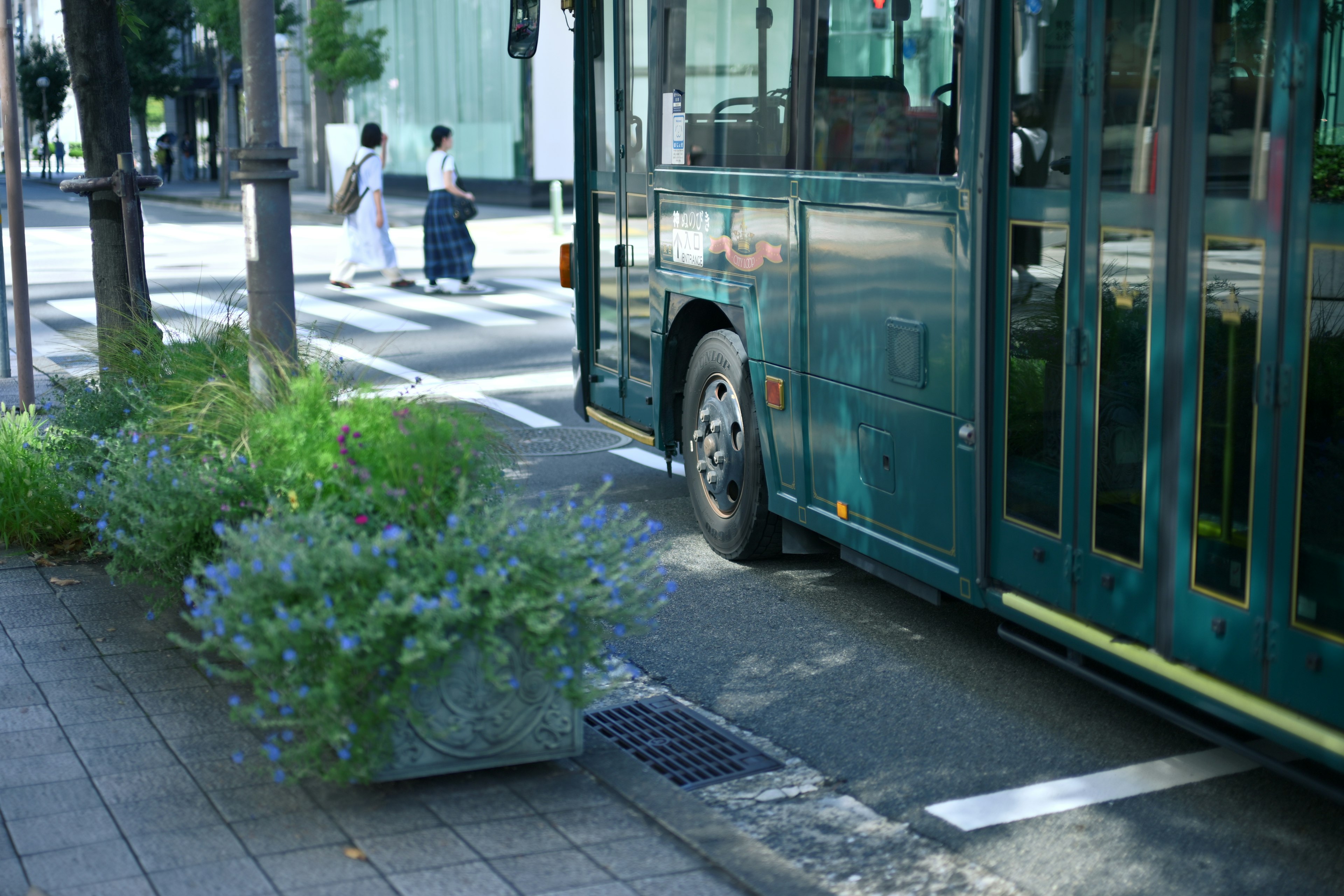 A green bus parked near a flower bed on a city street