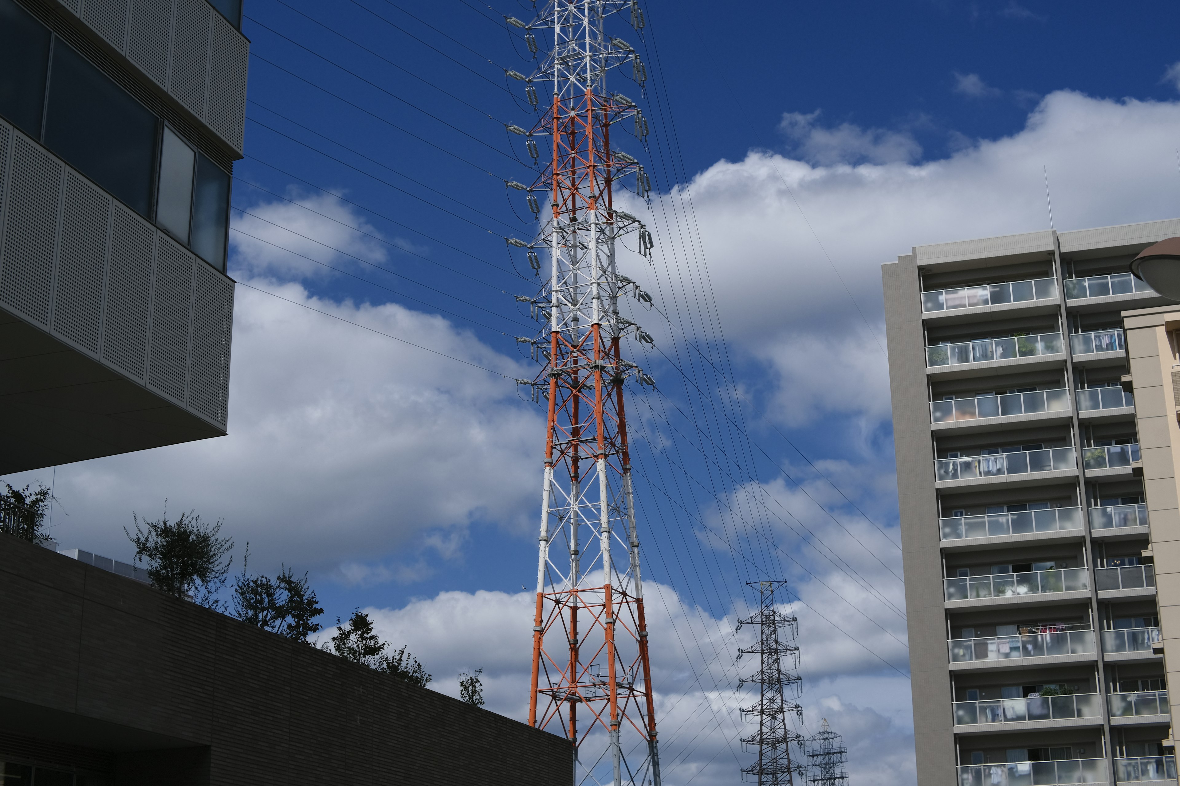 Torre di comunicazione rossa e bianca sotto un cielo blu con edifici vicini