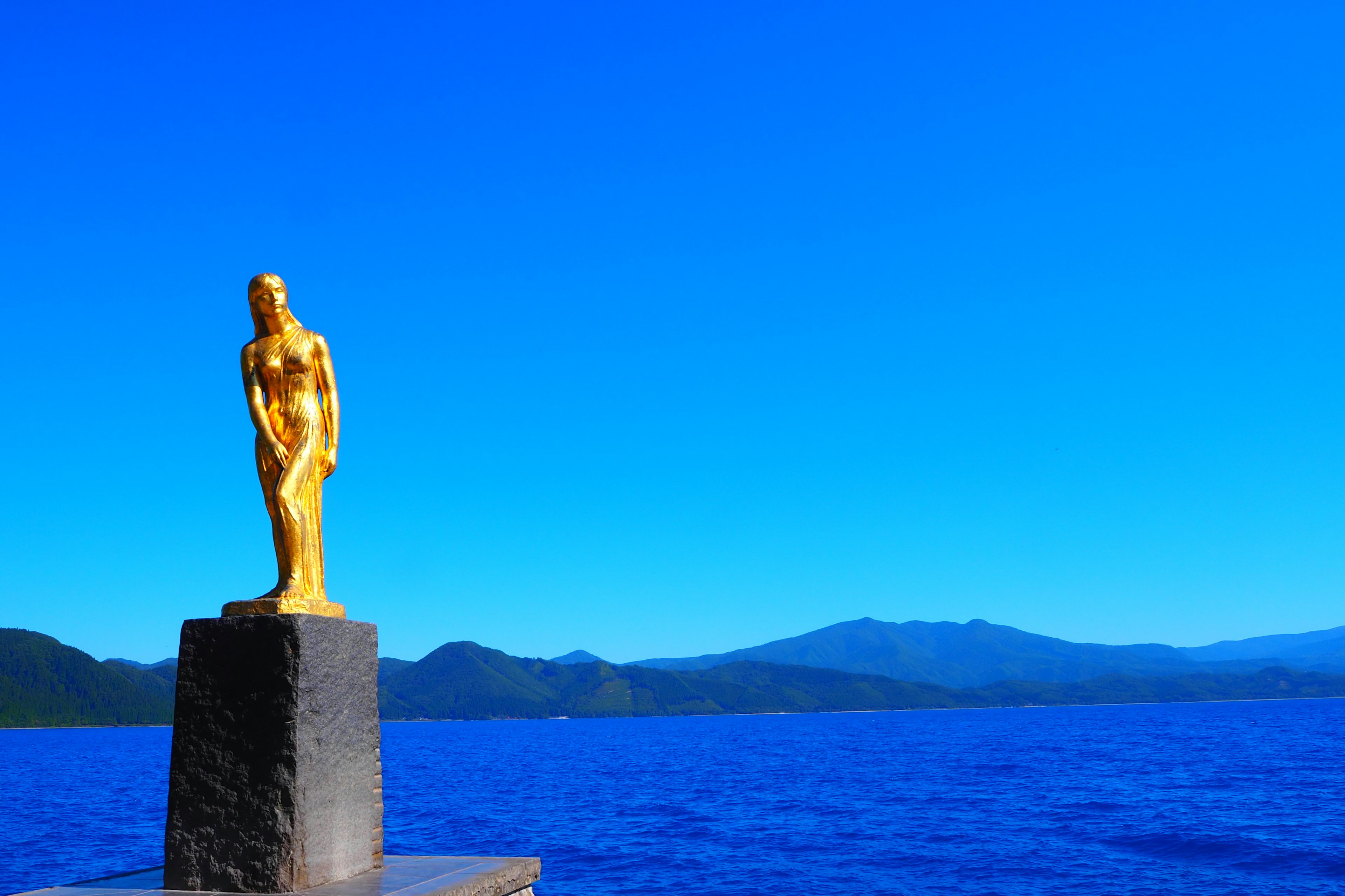 Patung emas dengan latar belakang laut biru dan pegunungan