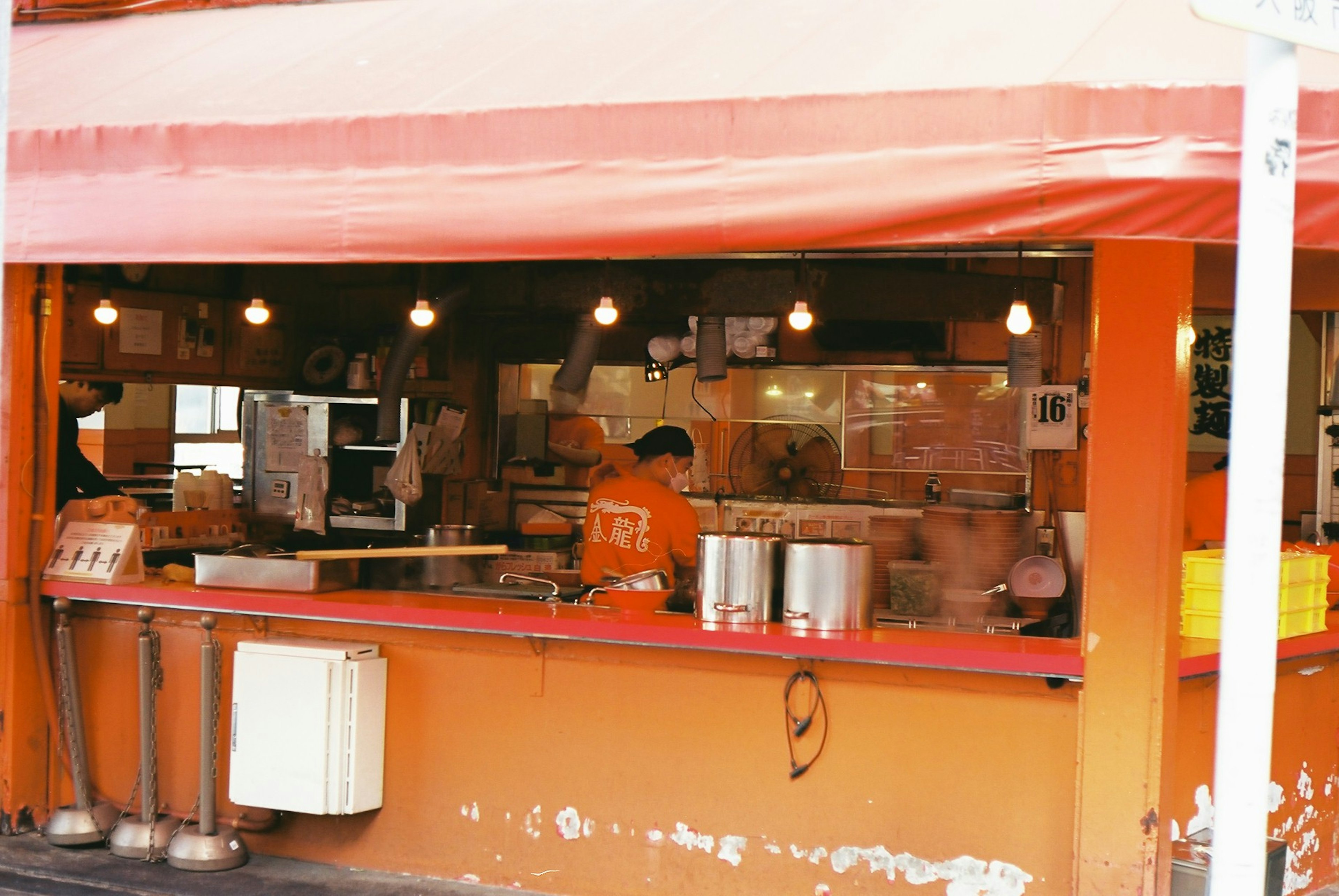 Chiosco di cibo arancione con personale che cucina sotto un awning rosso