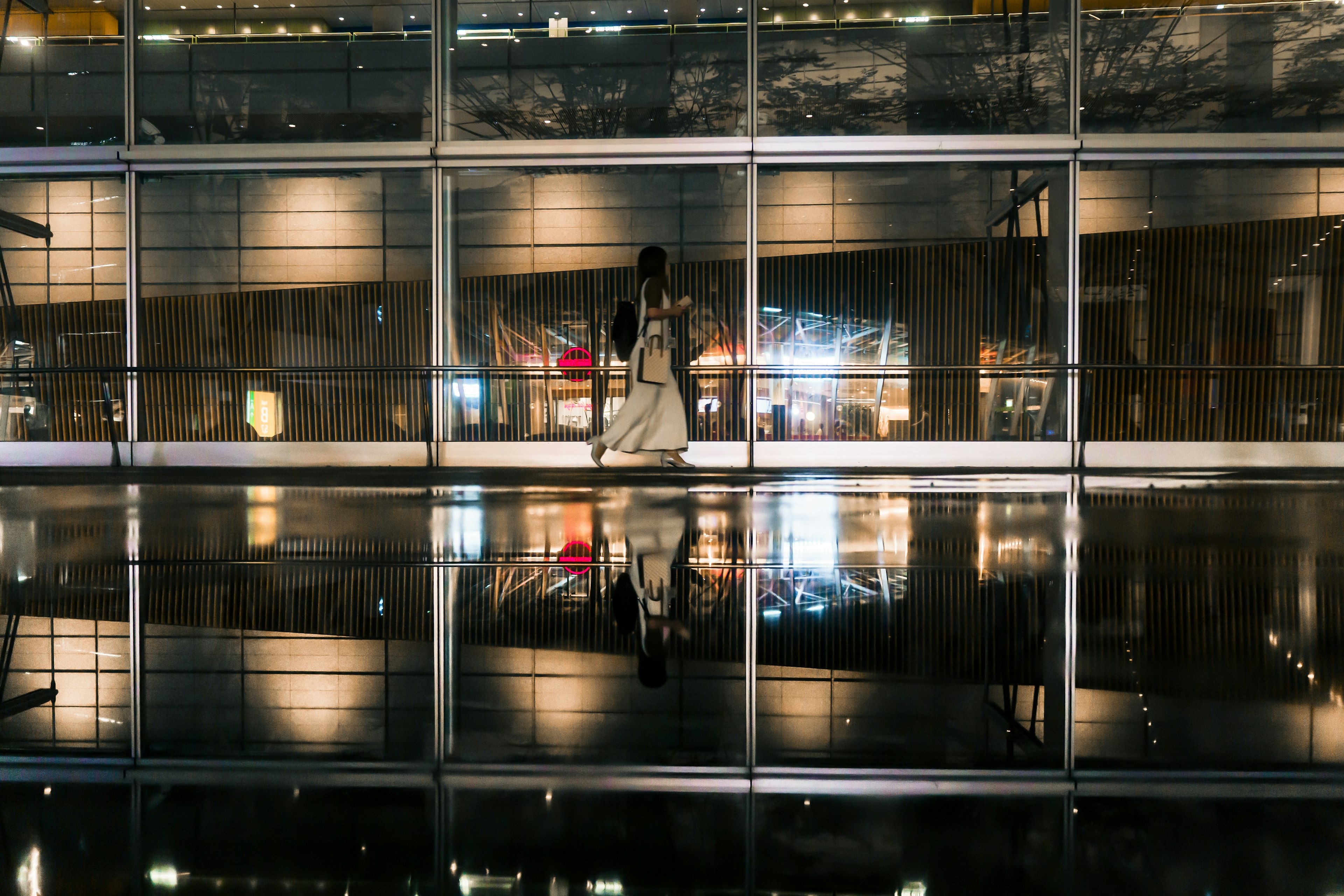 A woman in a white dress walking against a glass wall with reflections