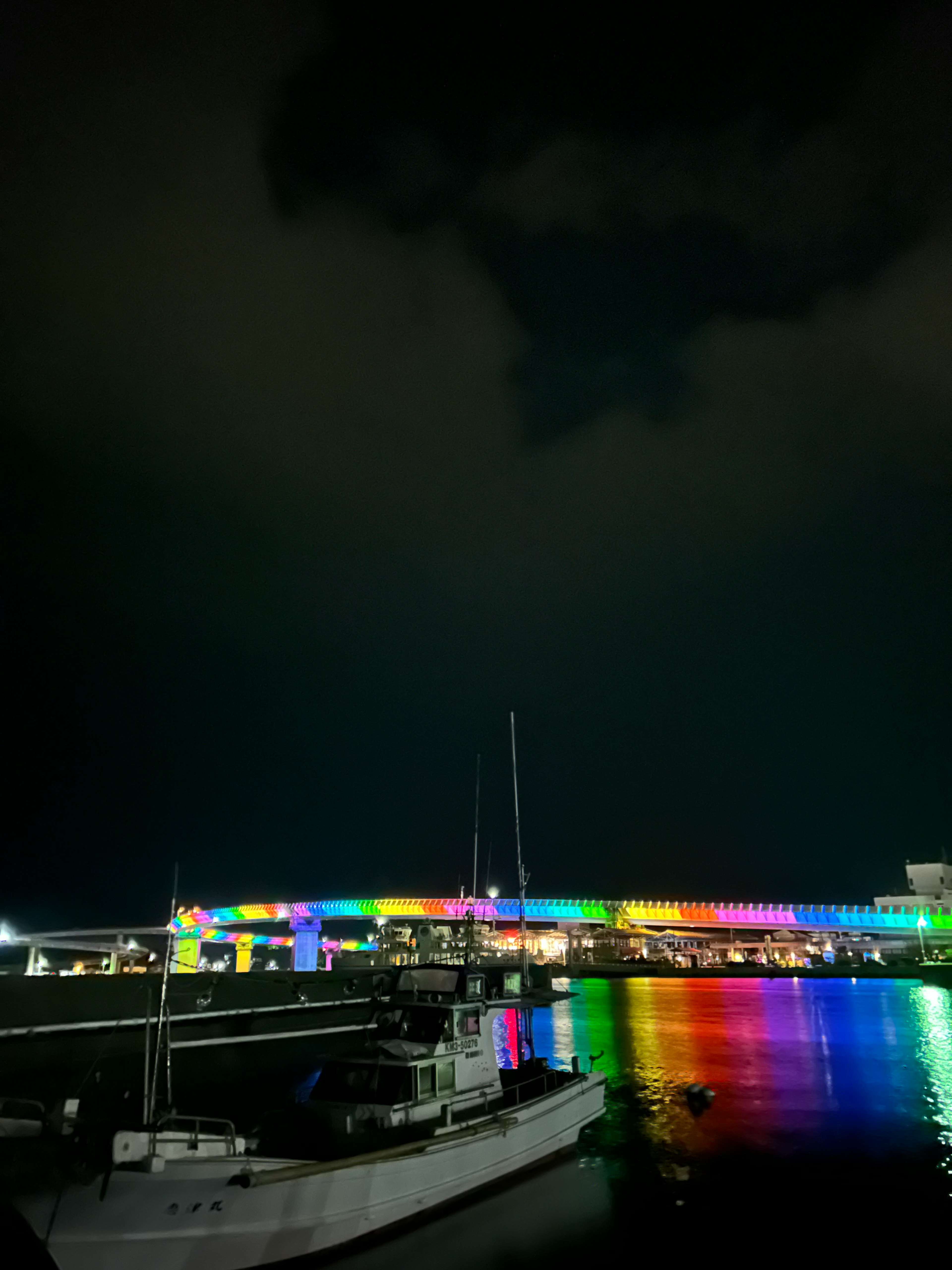 A boat in a harbor with a brightly lit rainbow bridge at night