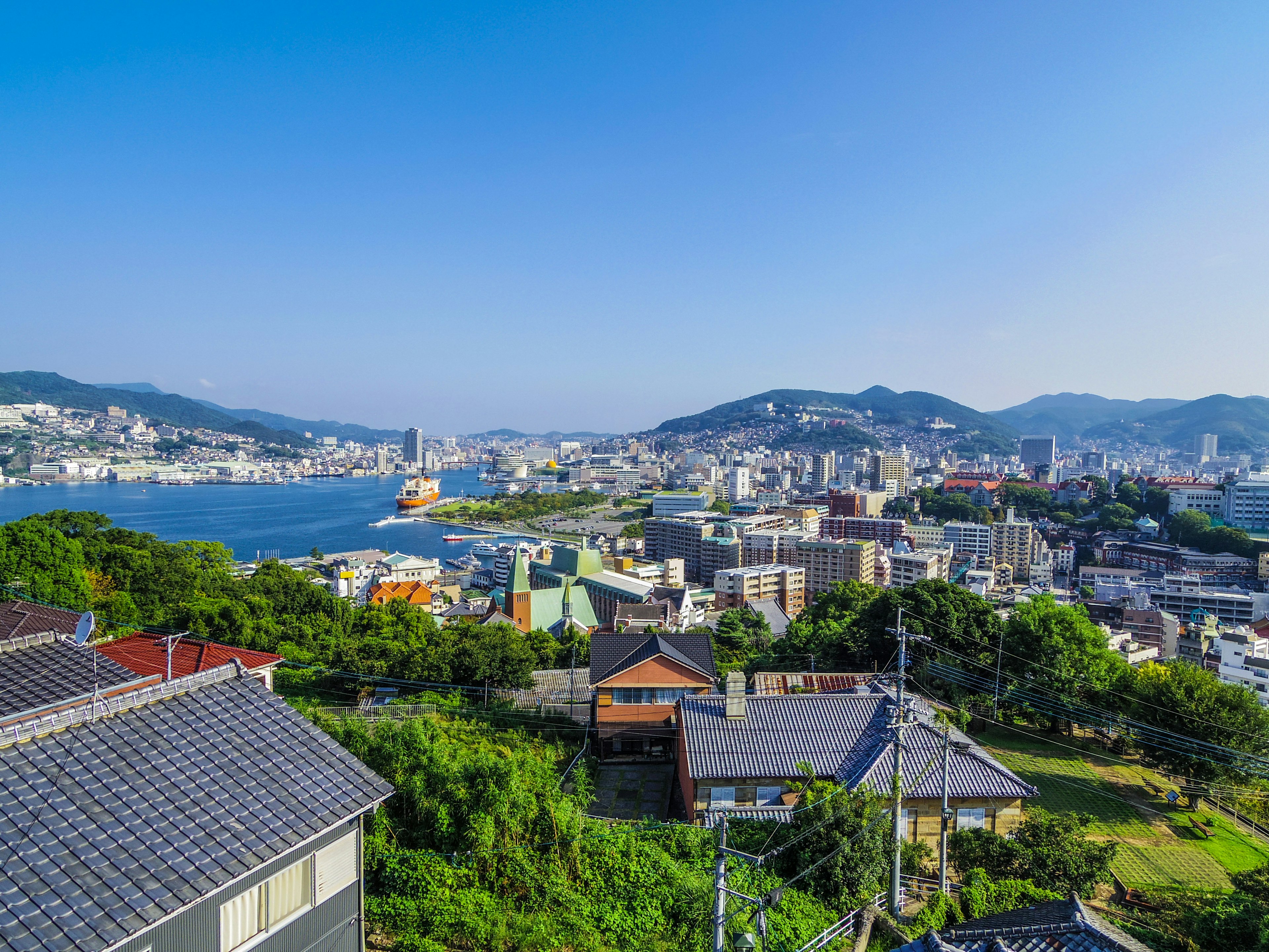 Vue panoramique d'une ville avec ciel bleu et collines vertes comprenant une rivière et des montagnes