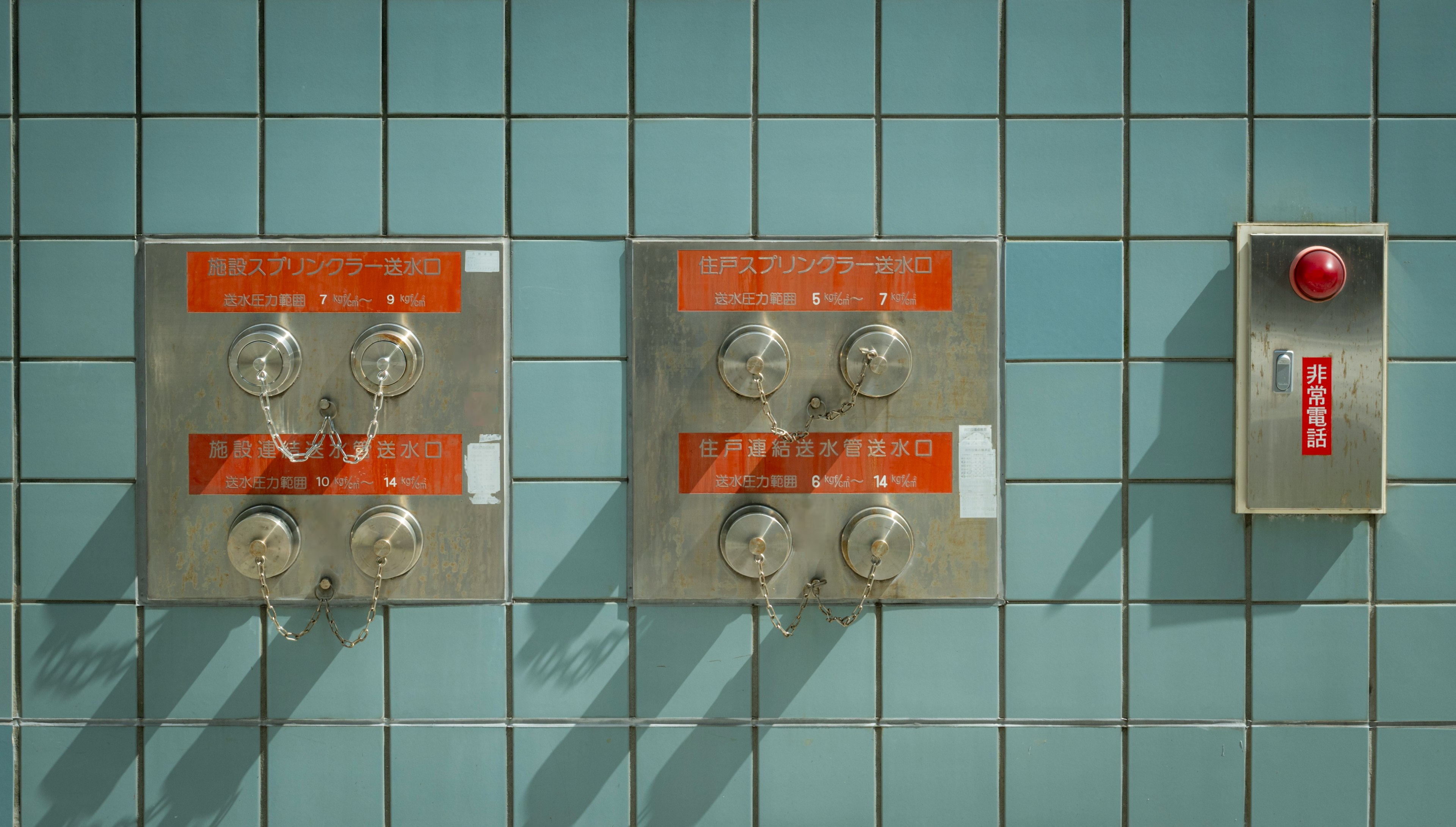 Metal fixtures mounted on a blue tiled wall with a red emergency button