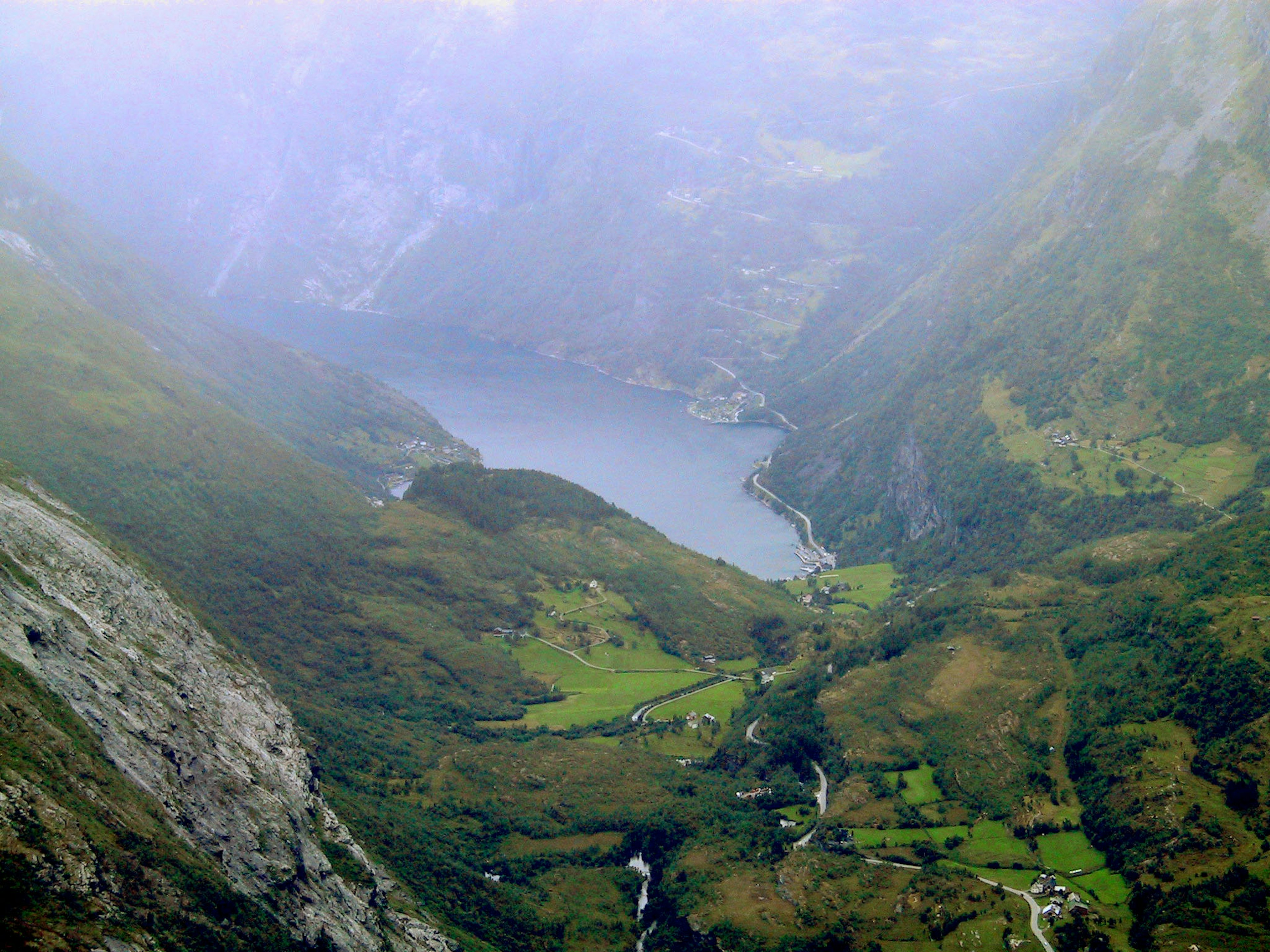 Misty mountain valley landscape with green fields and a visible lake