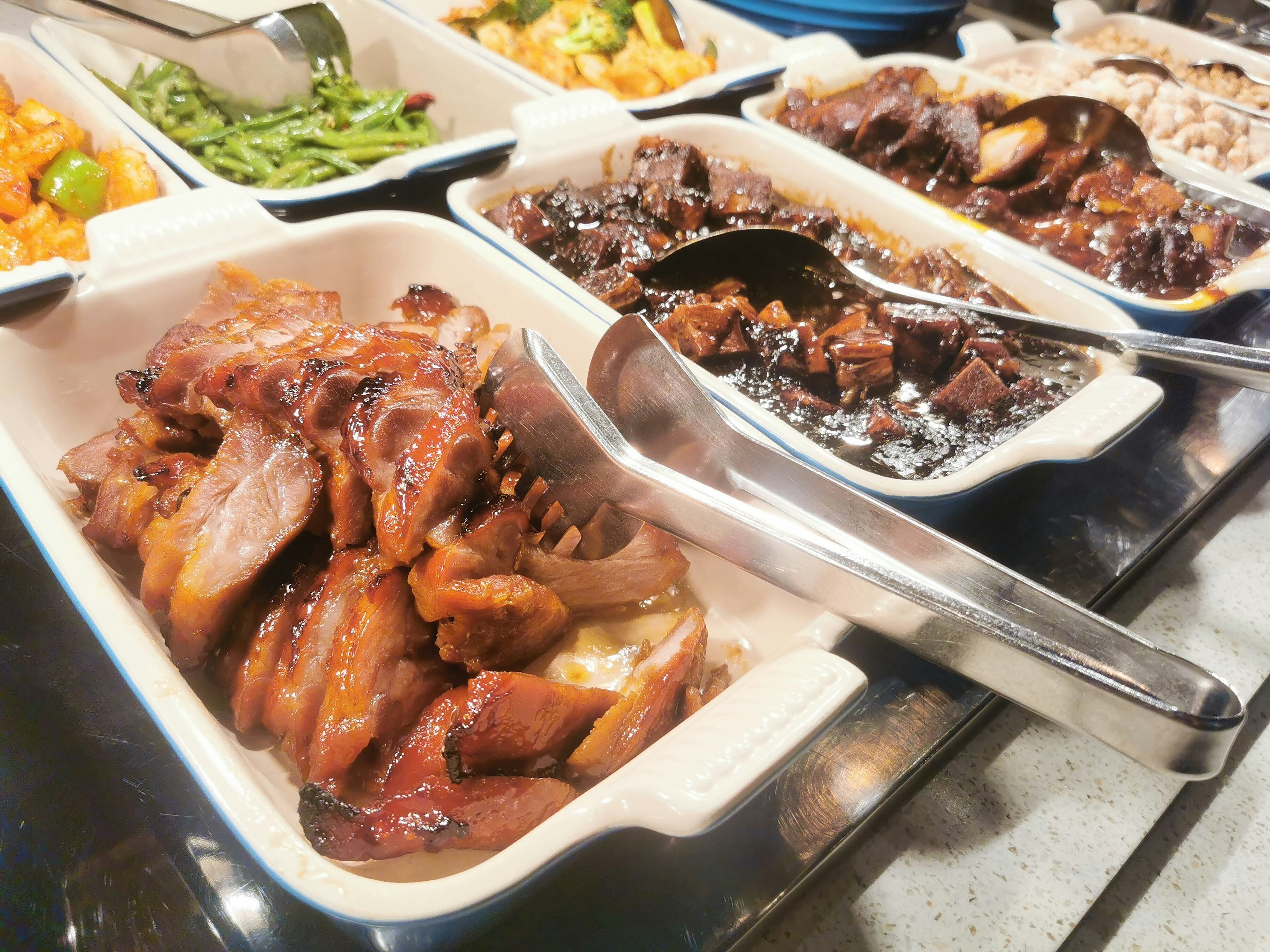 Buffet style table featuring glazed meats and stewed dishes