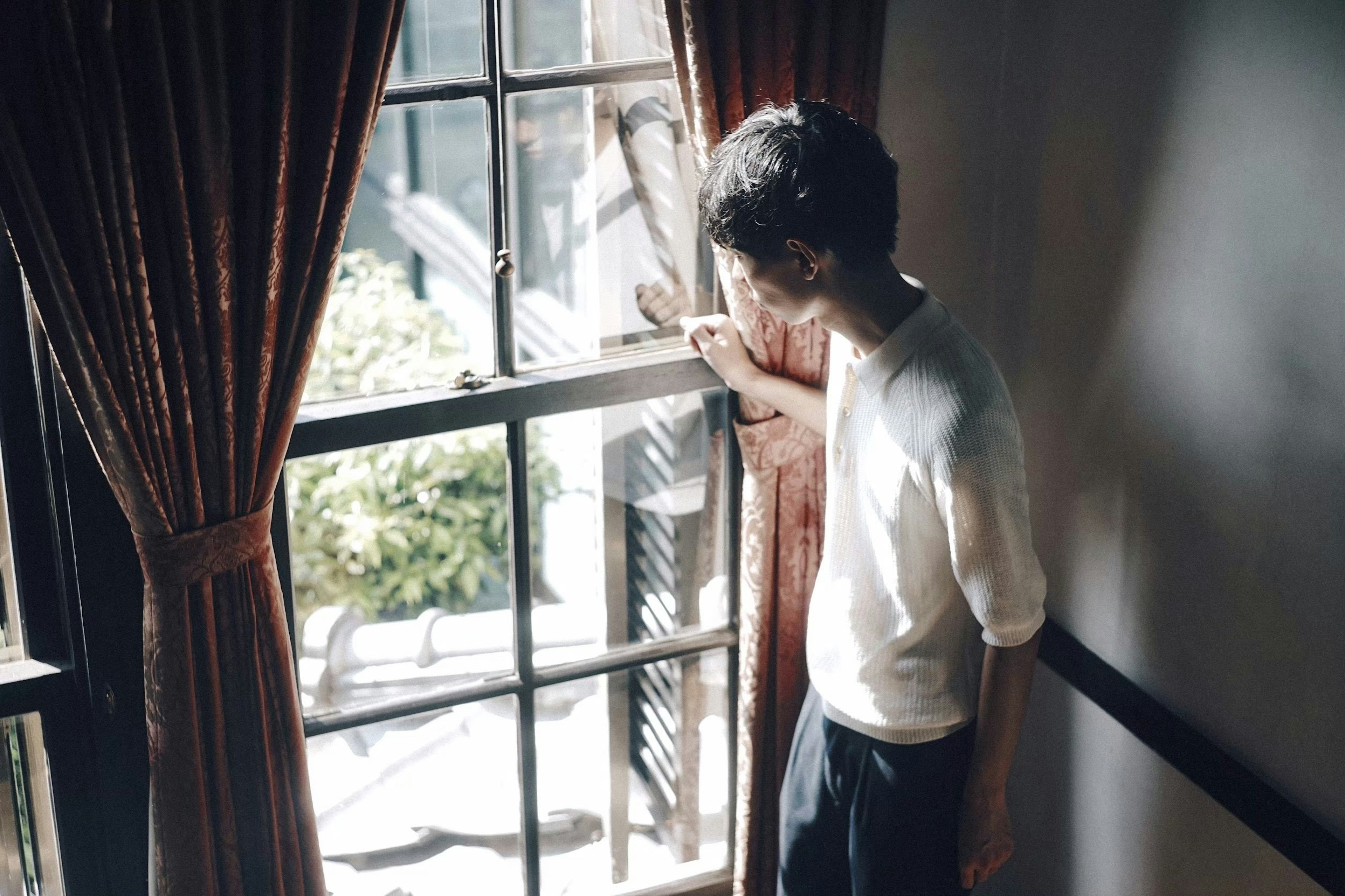 A person standing by a window with curtains in an interior room