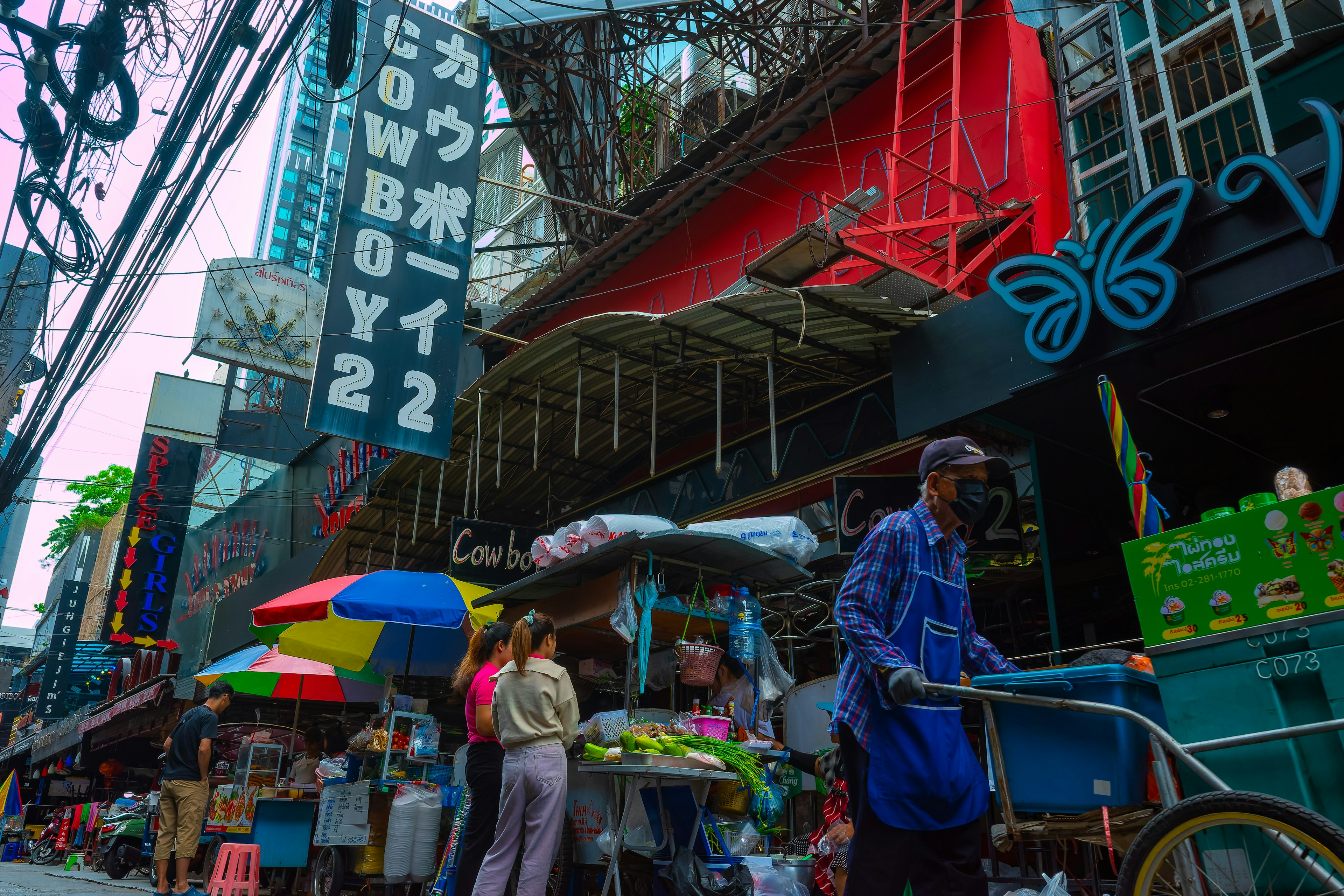 Cảnh chợ nhộn nhịp trên đường Cowboy ở Bangkok với các quầy hàng đầy màu sắc và người qua lại