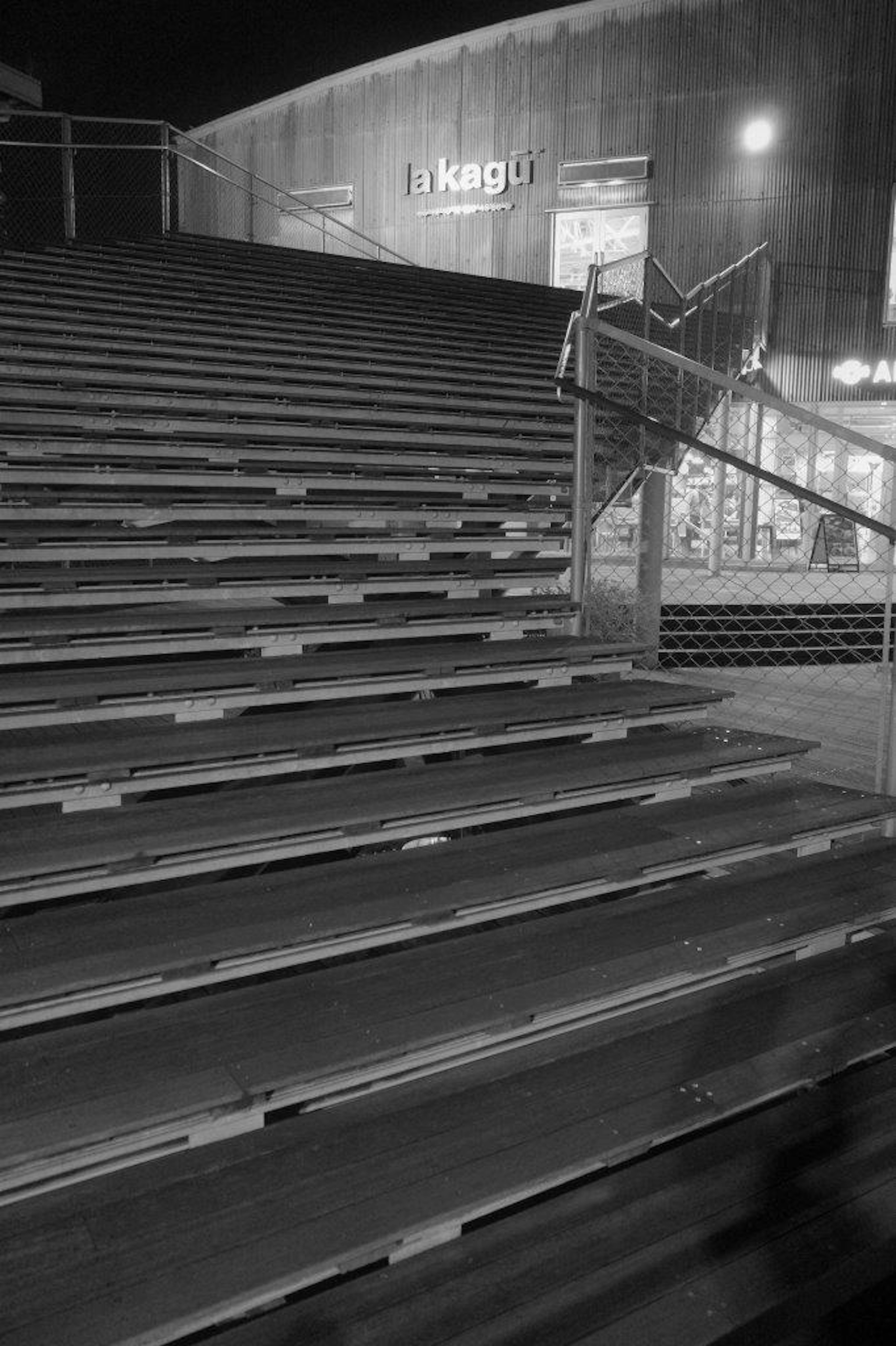 Foto en blanco y negro de escaleras por la noche con barandilla y luces de edificios circundantes