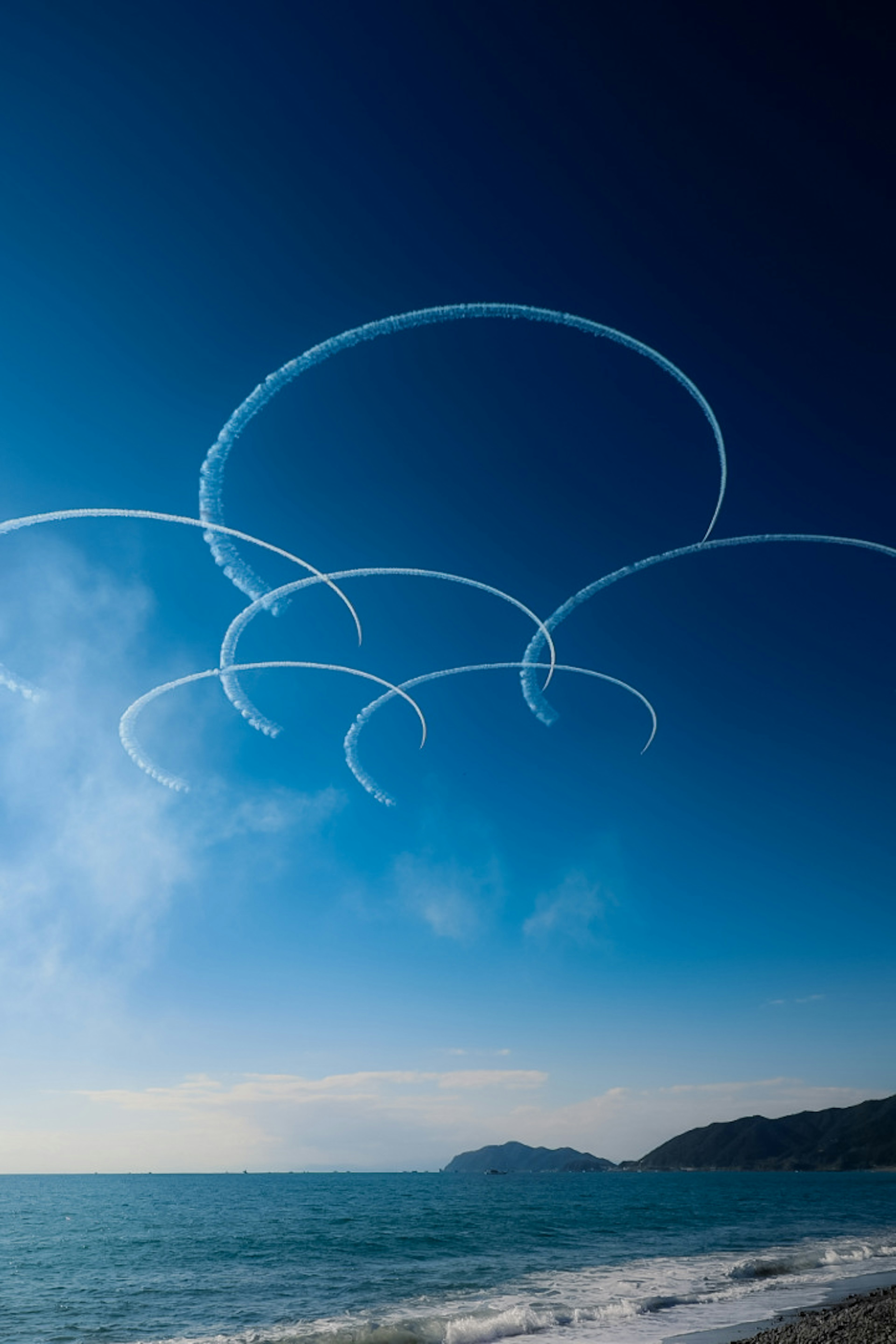 青空に描かれた飛行機雲の円形パターン海岸の風景